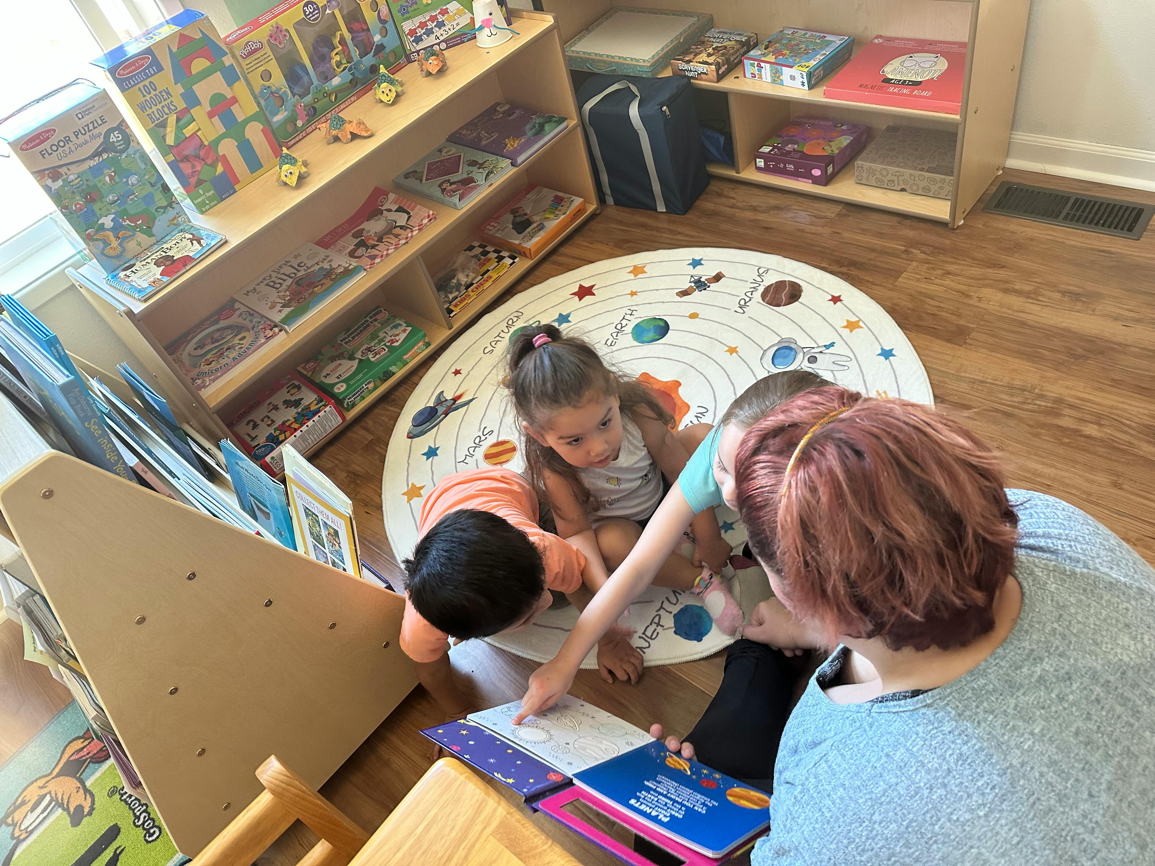 Adult and two children looking at a book on a rug