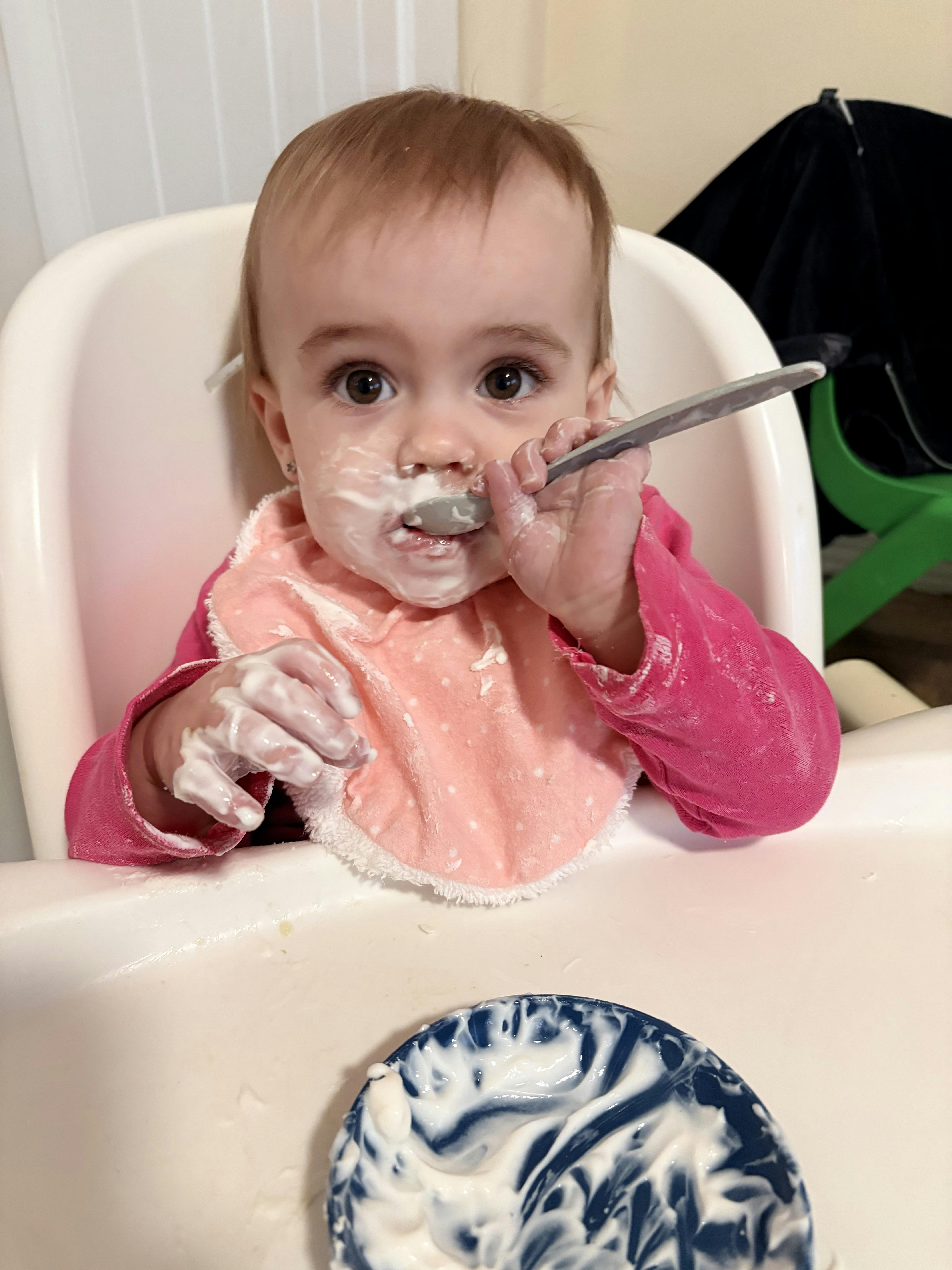 Child in a high chair eating from a spoon, face and hands covered in food