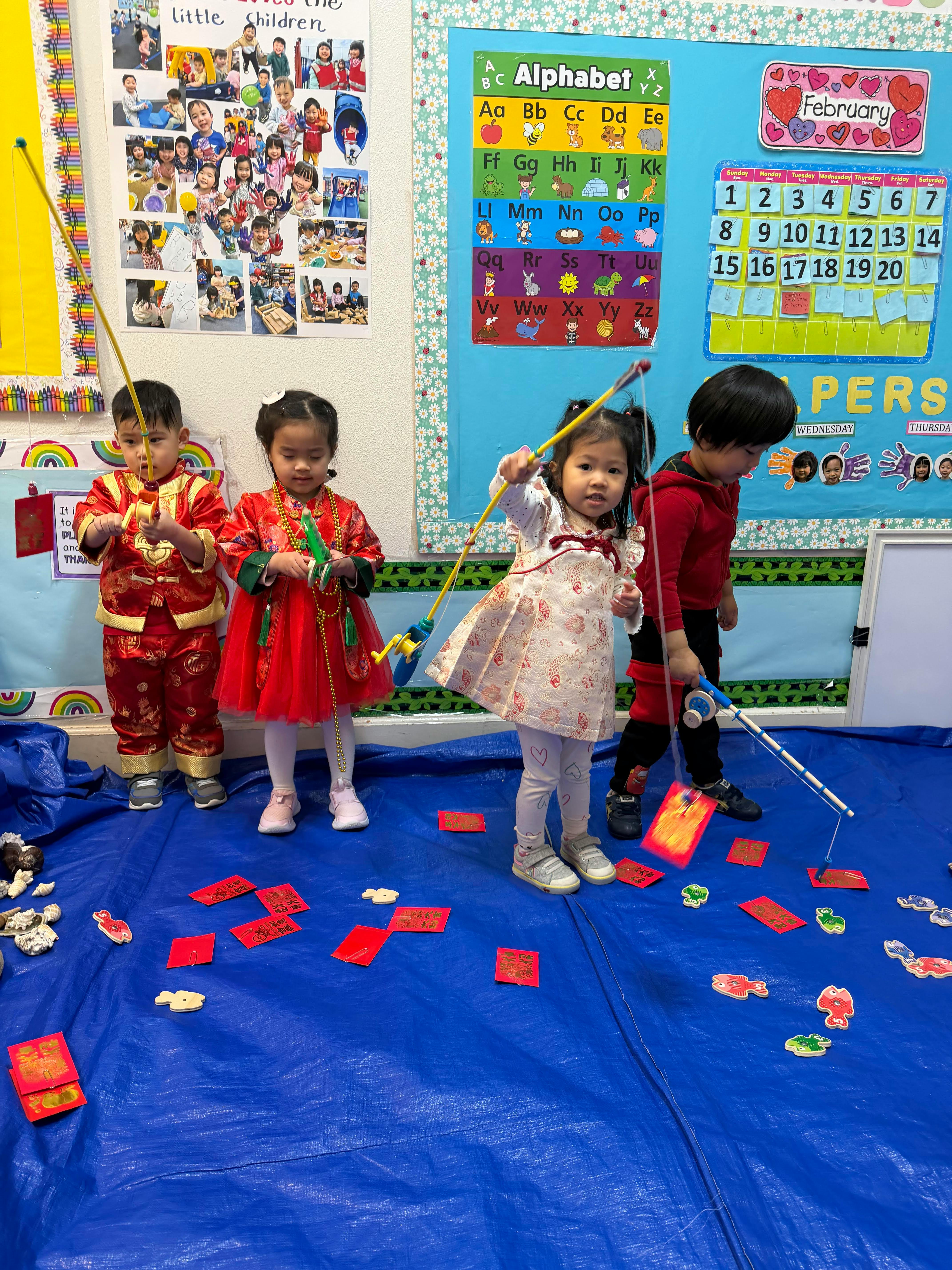 Four children playing a fishing game on a blue tarp in a classroom