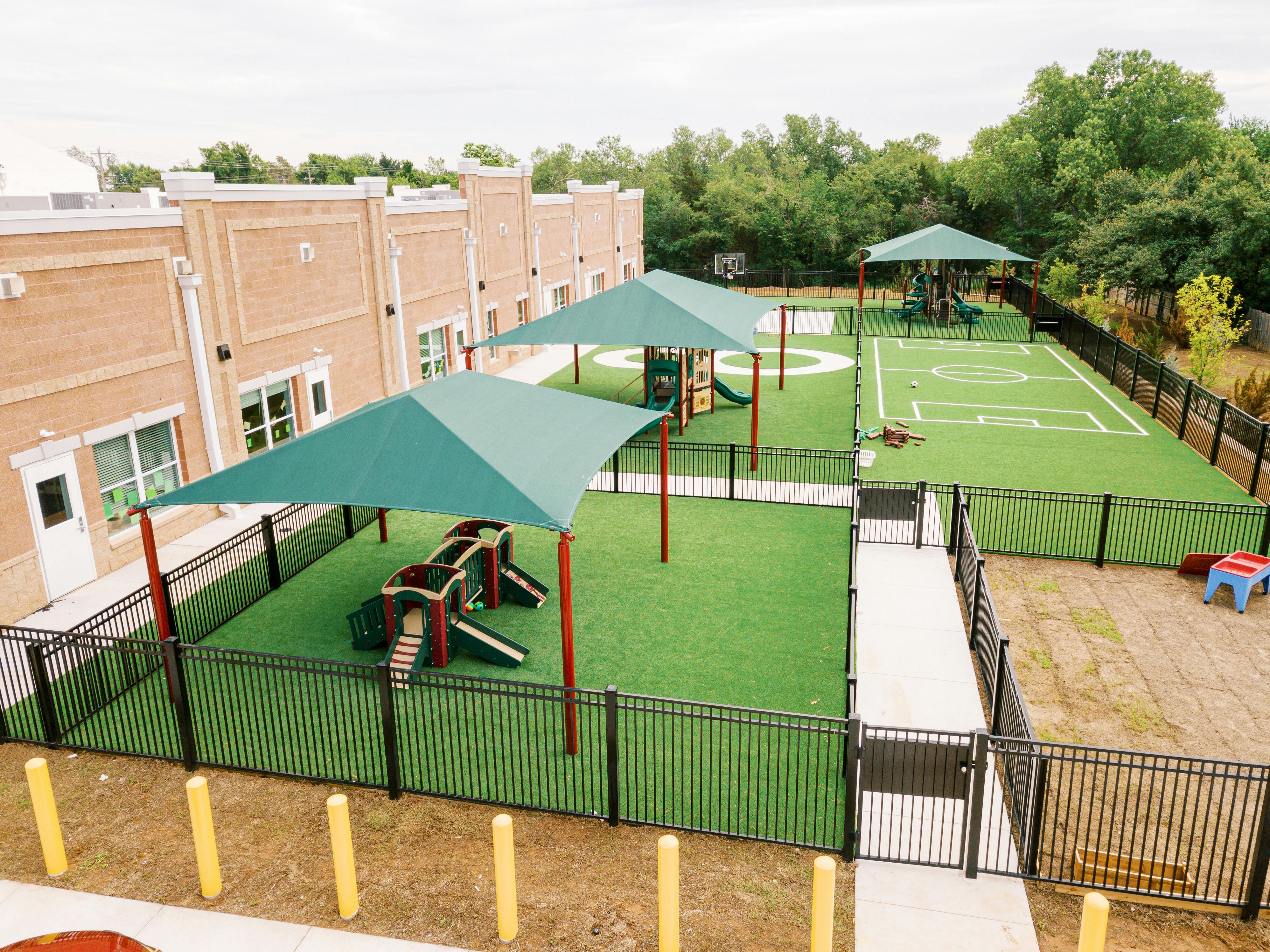 Outdoor playground with green turf, shade structures, and play equipment