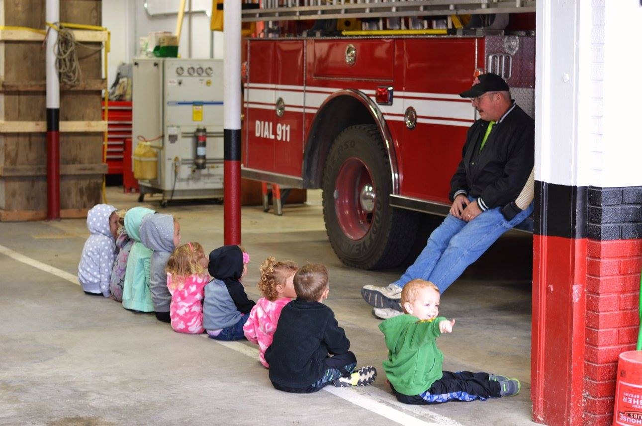 Adult sitting on a fire truck with children sitting on the floor in front