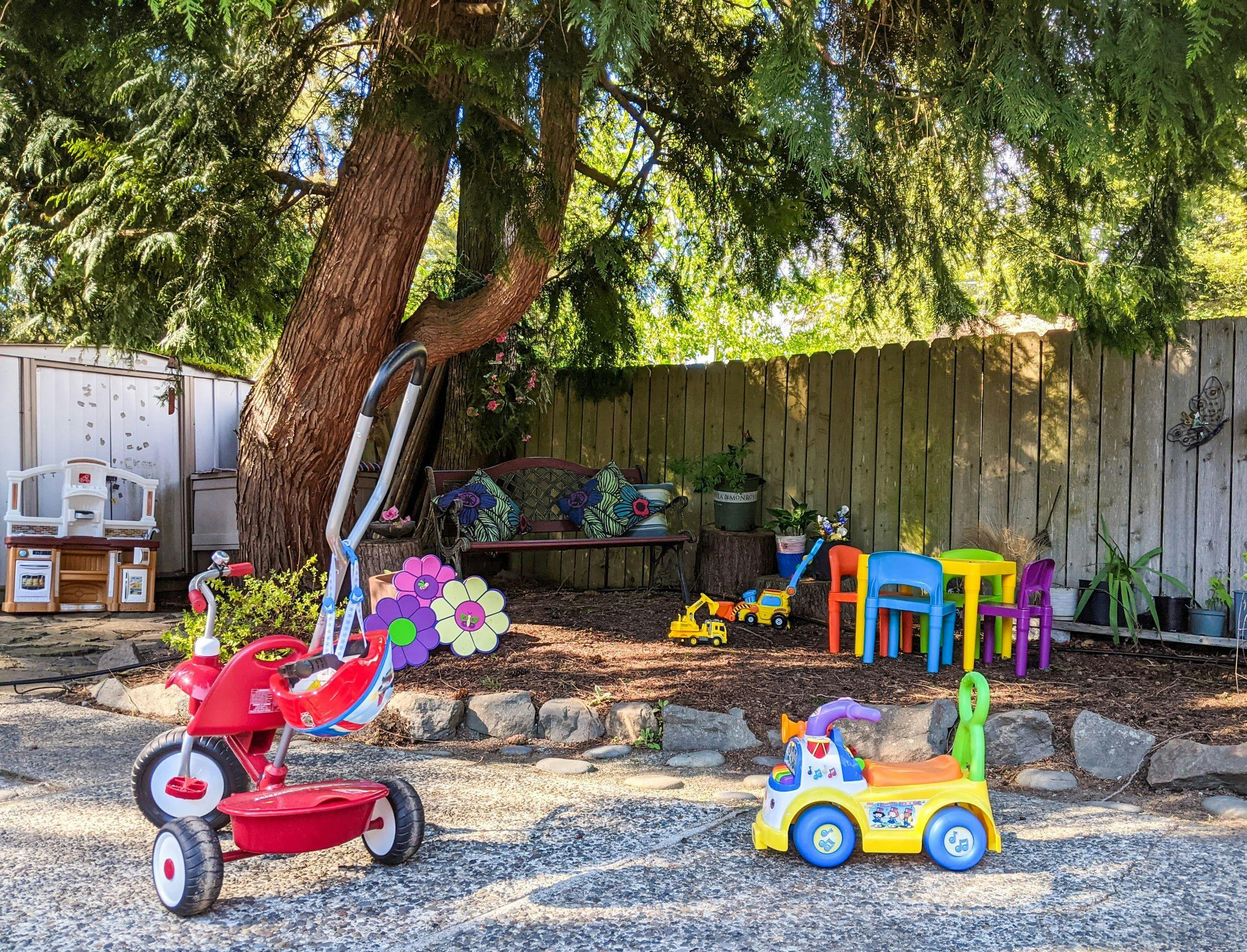 Red tricycle and yellow toy truck in a play area under a tree