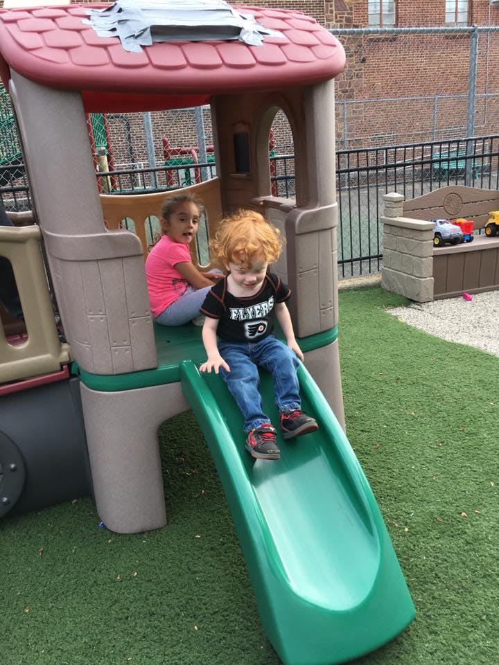 Two children on a playground structure, one on a slide