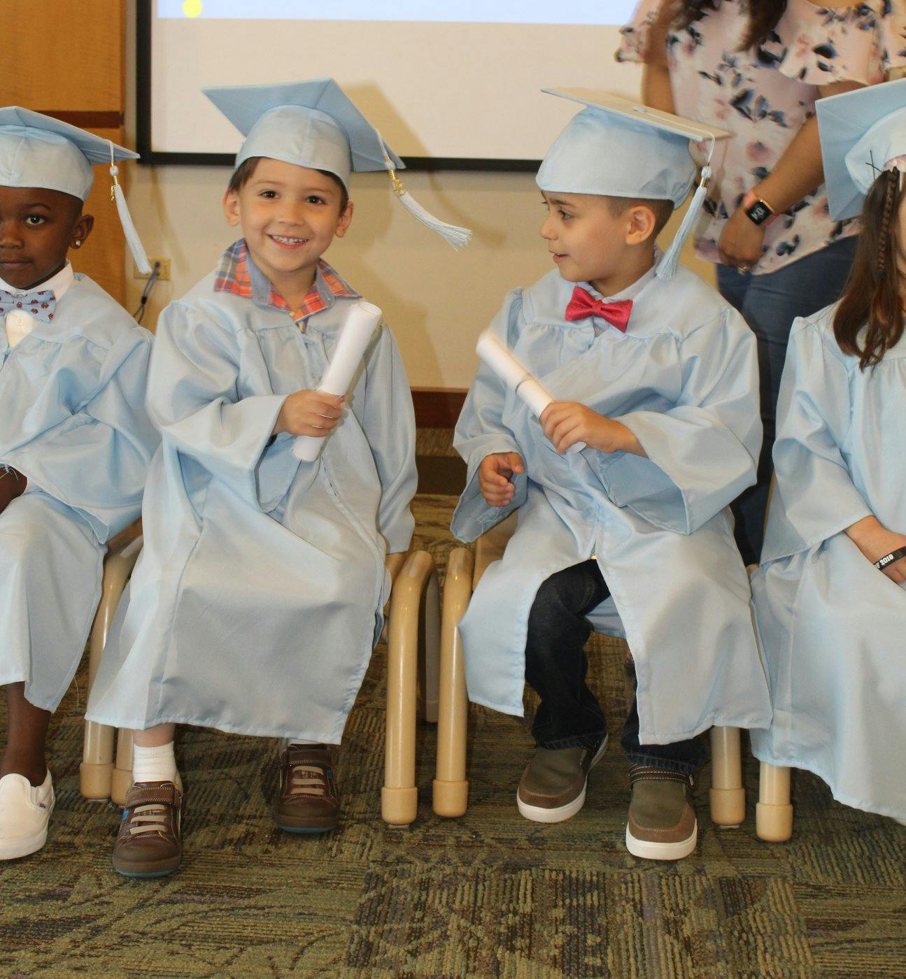Children in light blue graduation caps and gowns holding diplomas