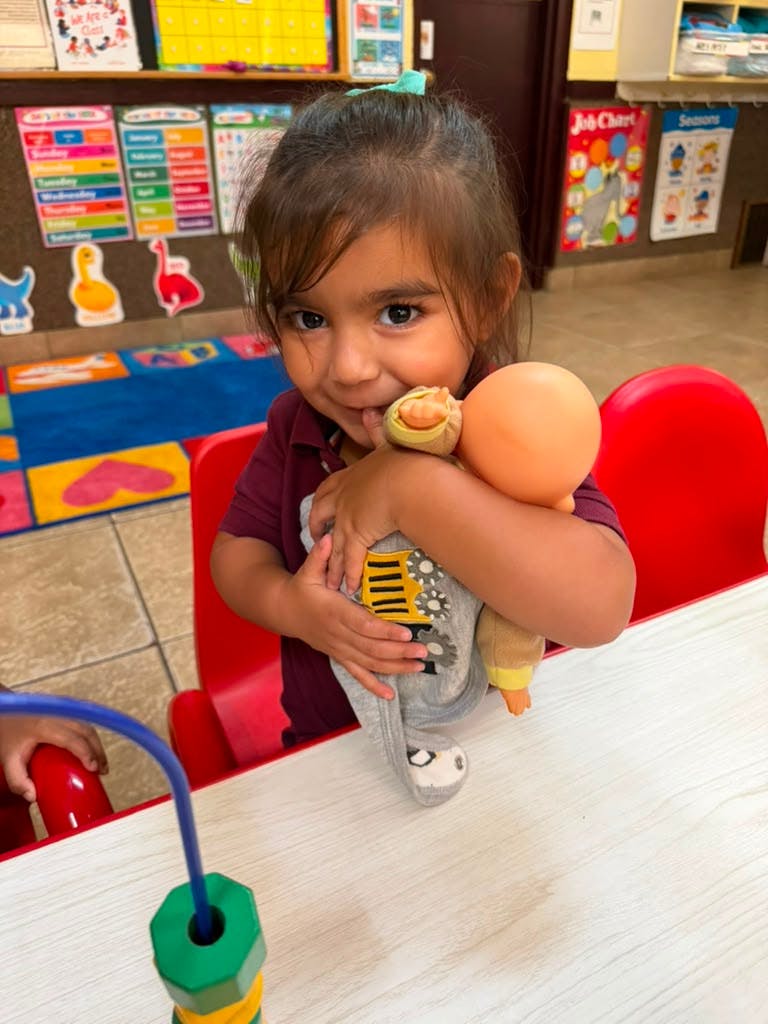 Child hugging a doll in a classroom