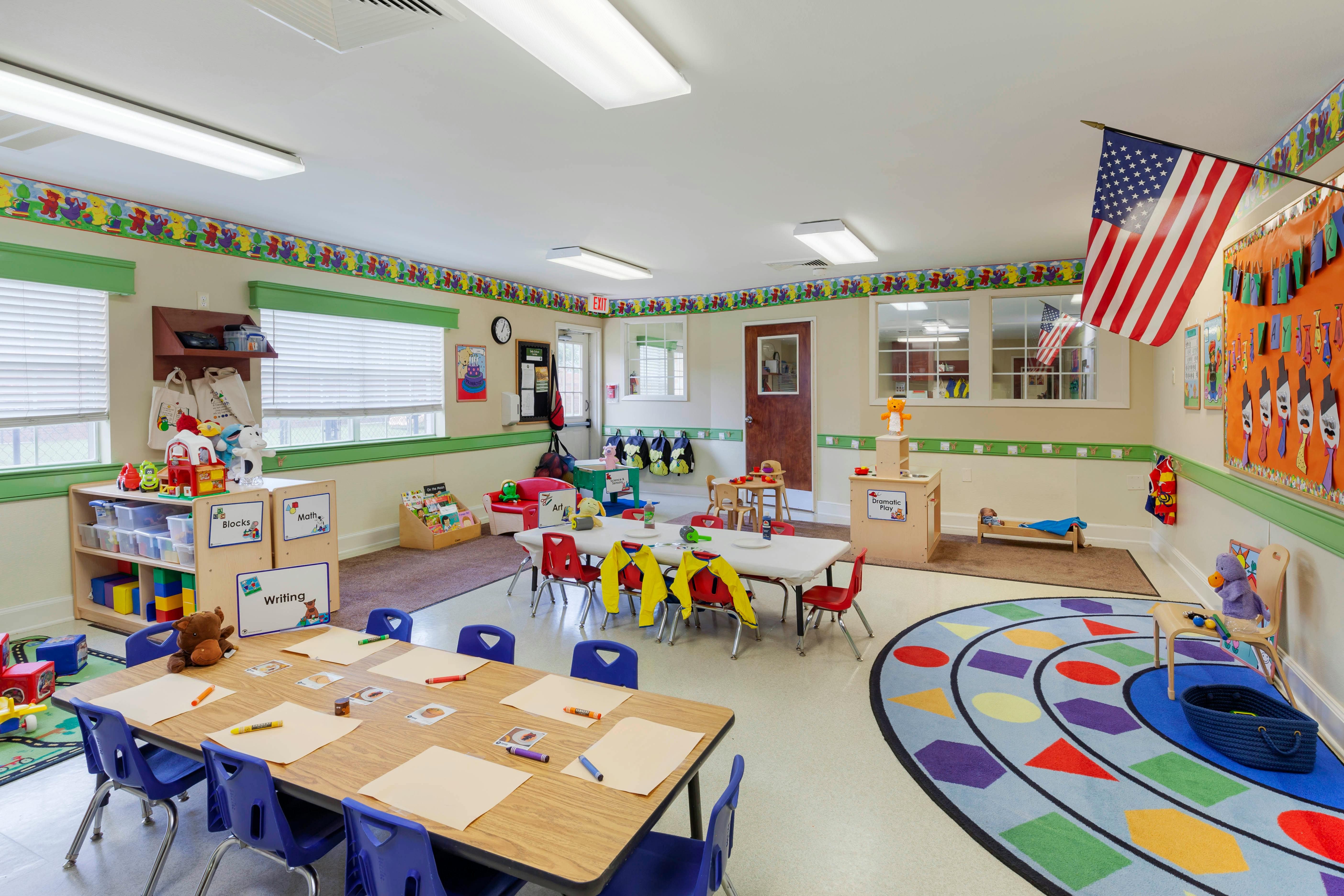 Classroom with tables, chairs, colorful rugs, toys, and educational materials