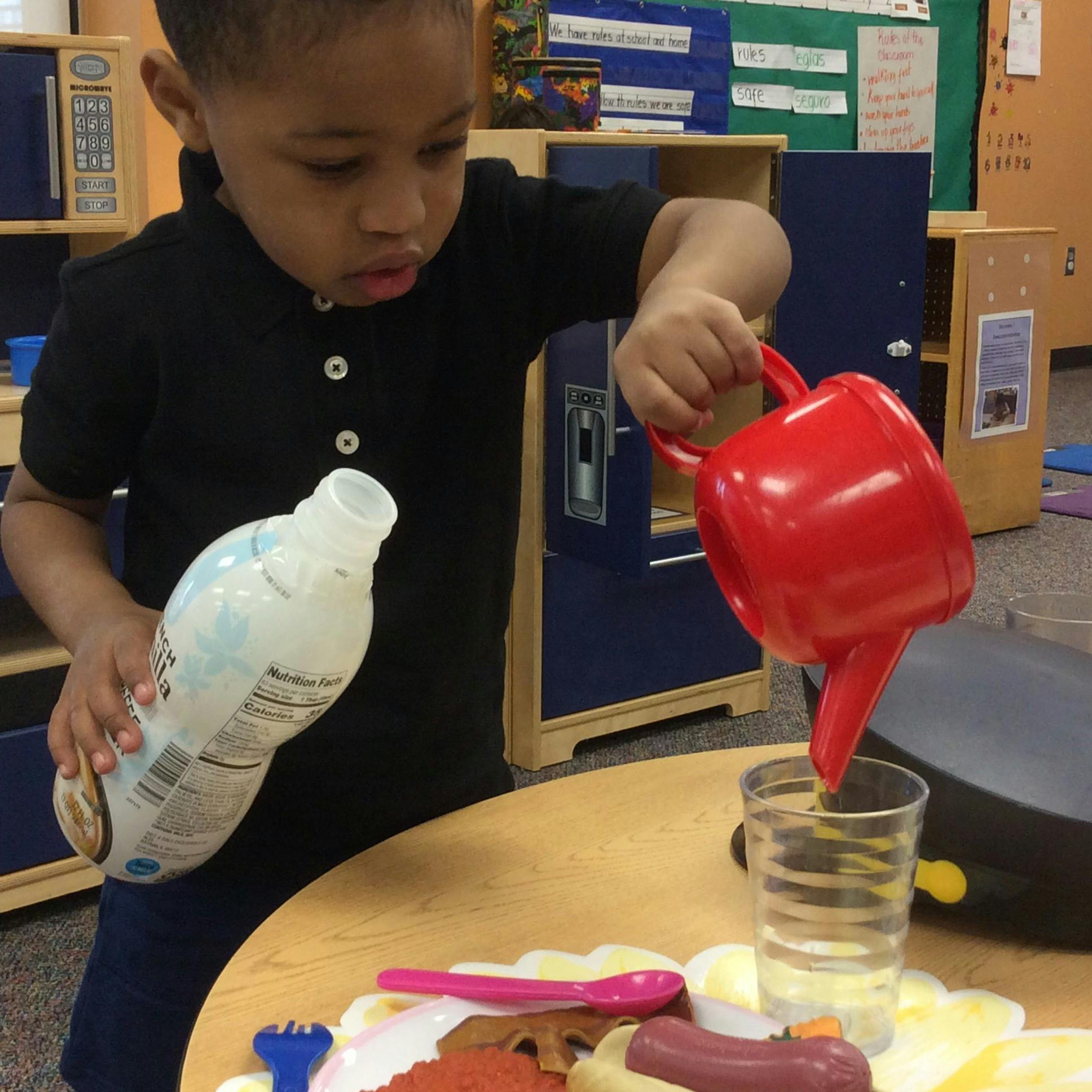 Child pouring from a red watering can into a clear cup