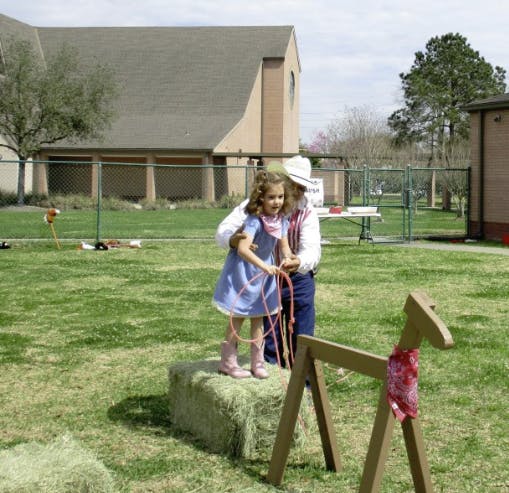 Person in cowboy hat helping child on hay bale with rope
