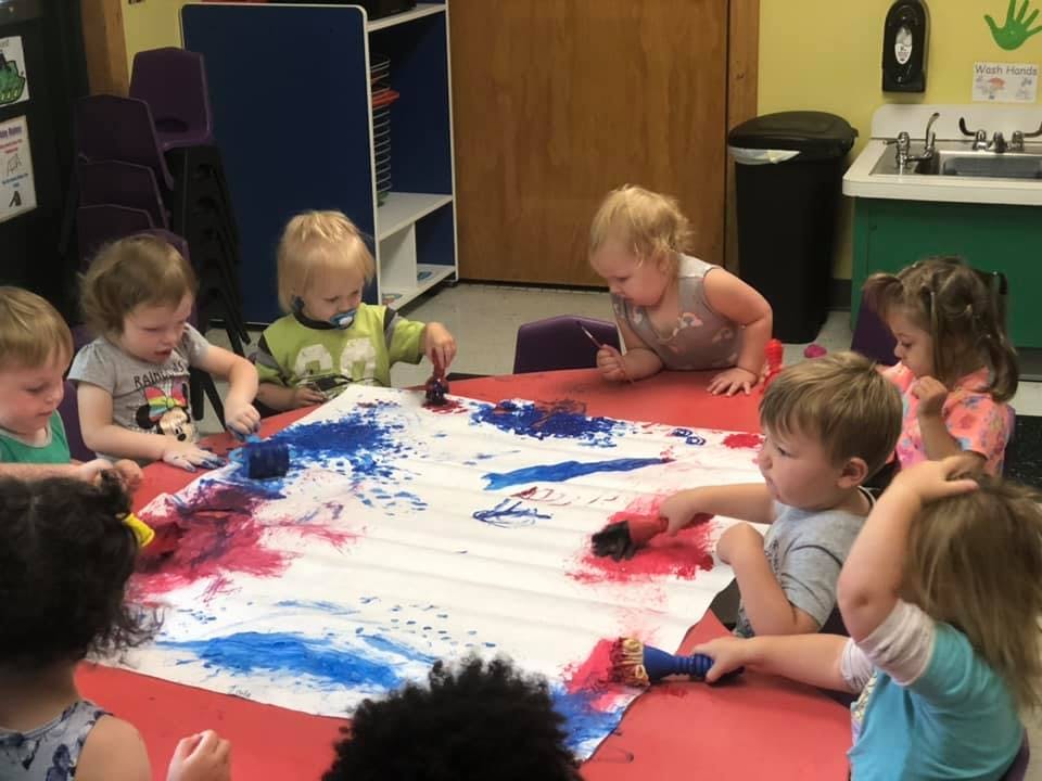 Children painting on a large white sheet on a red table