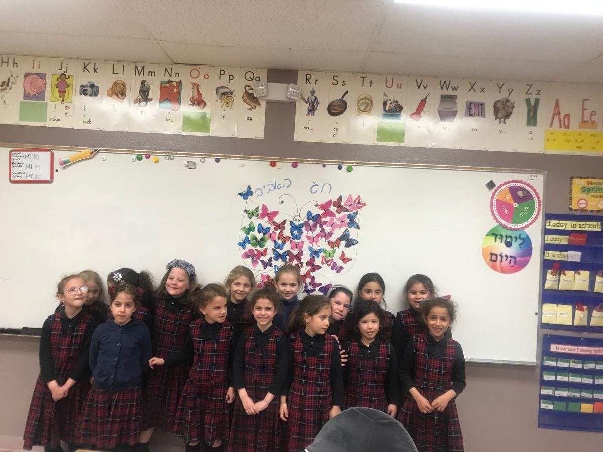 Children standing in a classroom in front of a whiteboard with butterfly decorations