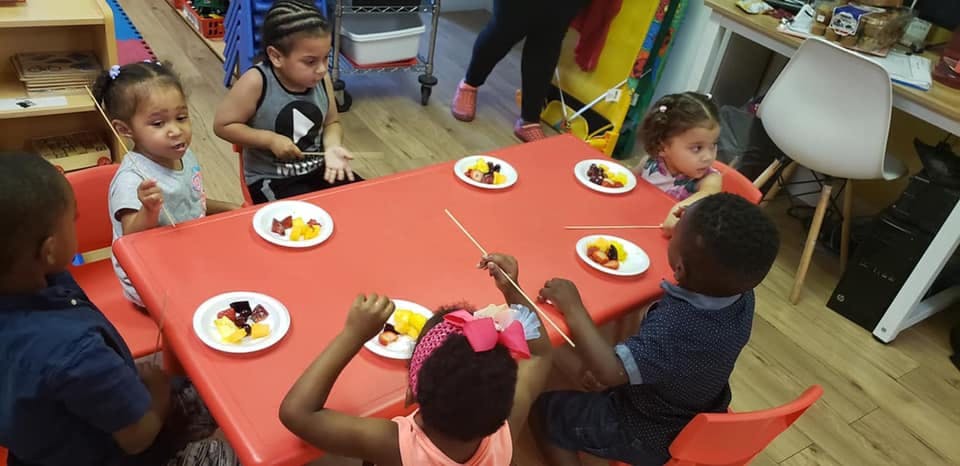 Children sitting at a table with plates of fruit