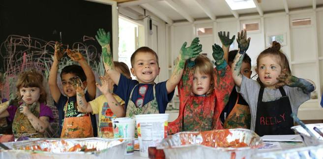 Children with paint on their hands and aprons raising their arms
