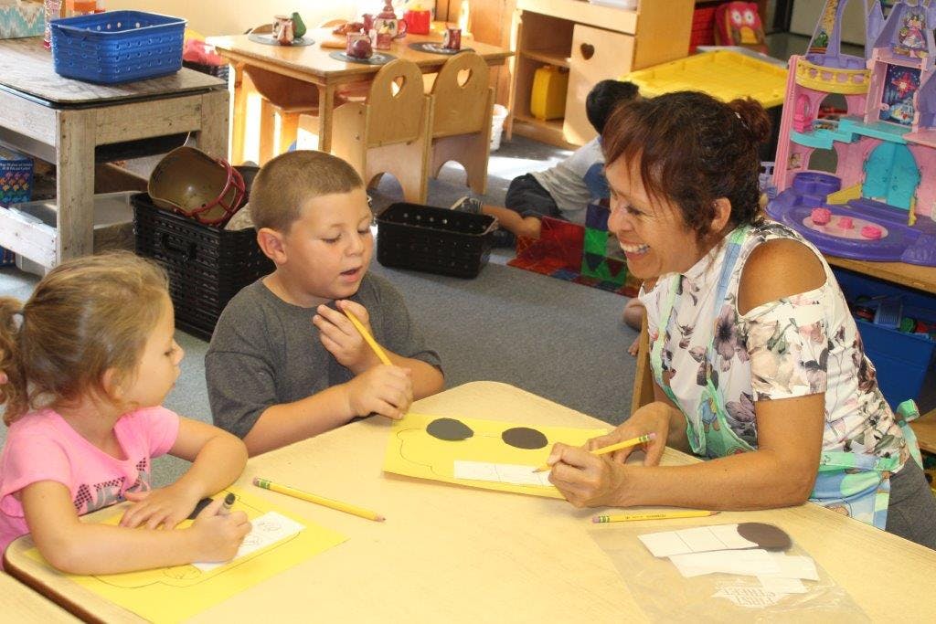 Adult and two children drawing at a table in a classroom