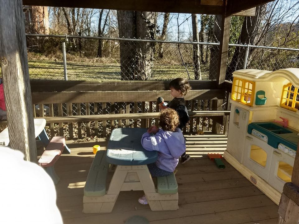 Two children playing on a wooden deck with a toy kitchen and picnic table