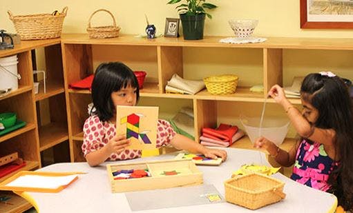 Two children playing with puzzles at a table in a classroom