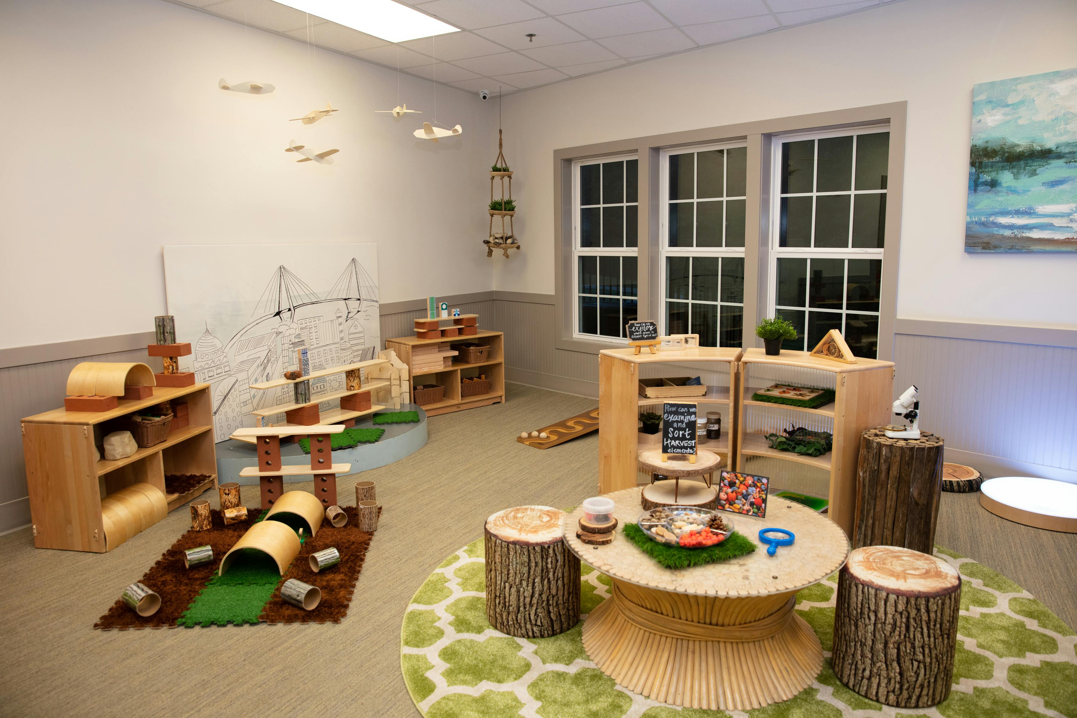 Classroom with wooden play structures, shelves, and a round table with tree stump seats