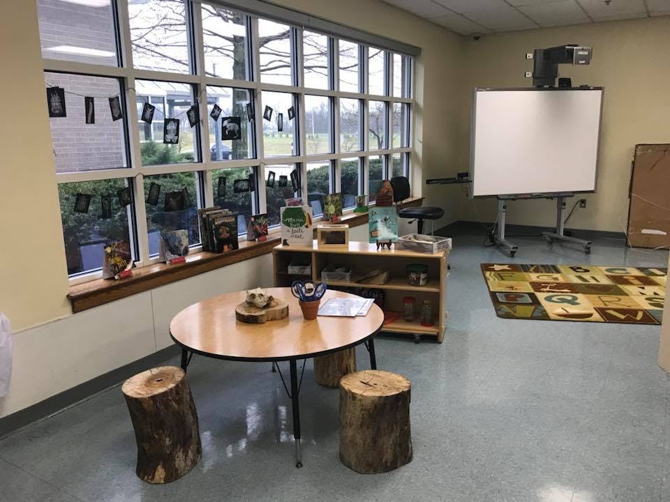 Classroom with a round table, tree stump seats, and large windows
