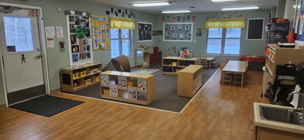 Empty classroom with small tables and chairs, shelves, and decorations on walls