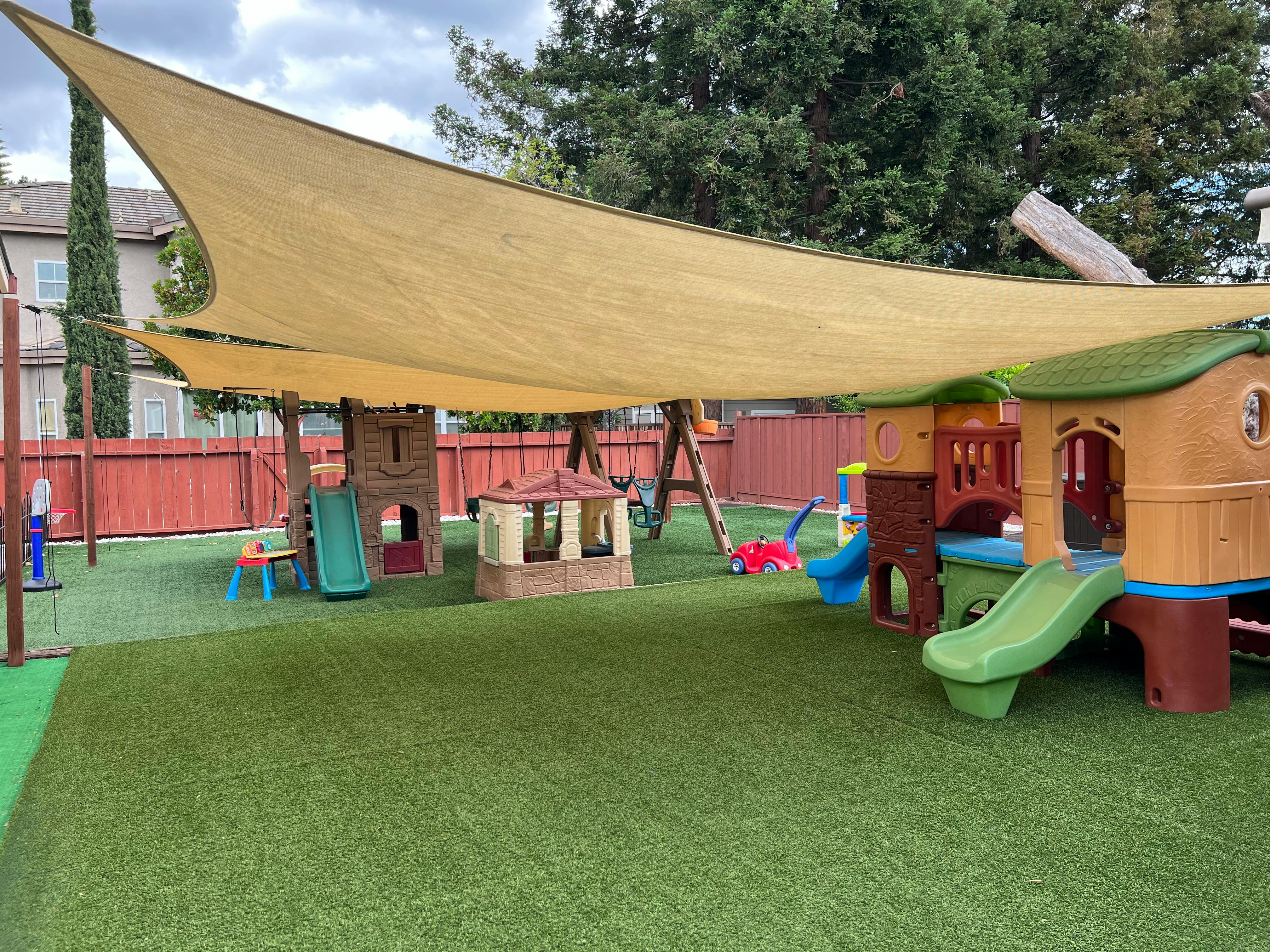 Outdoor playground with play structures, slides, and a swing set under a shade sail
