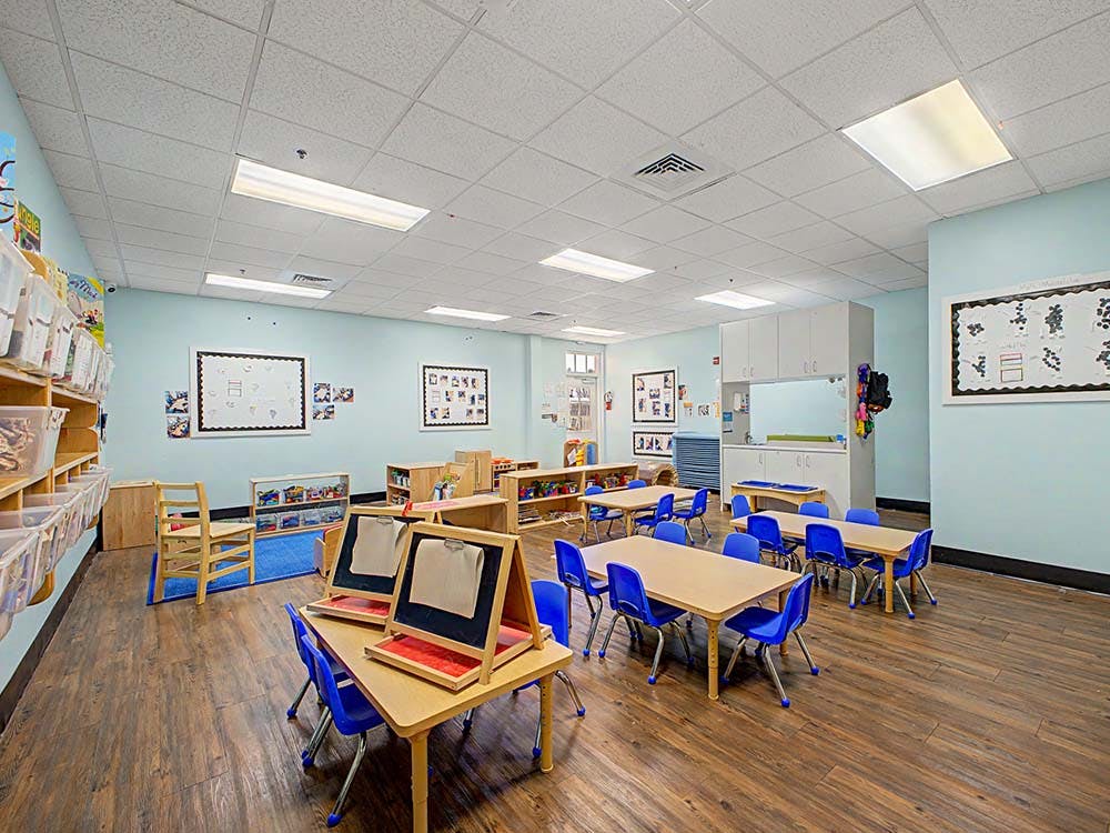 Empty classroom with small tables, blue chairs, storage shelves, and easels
