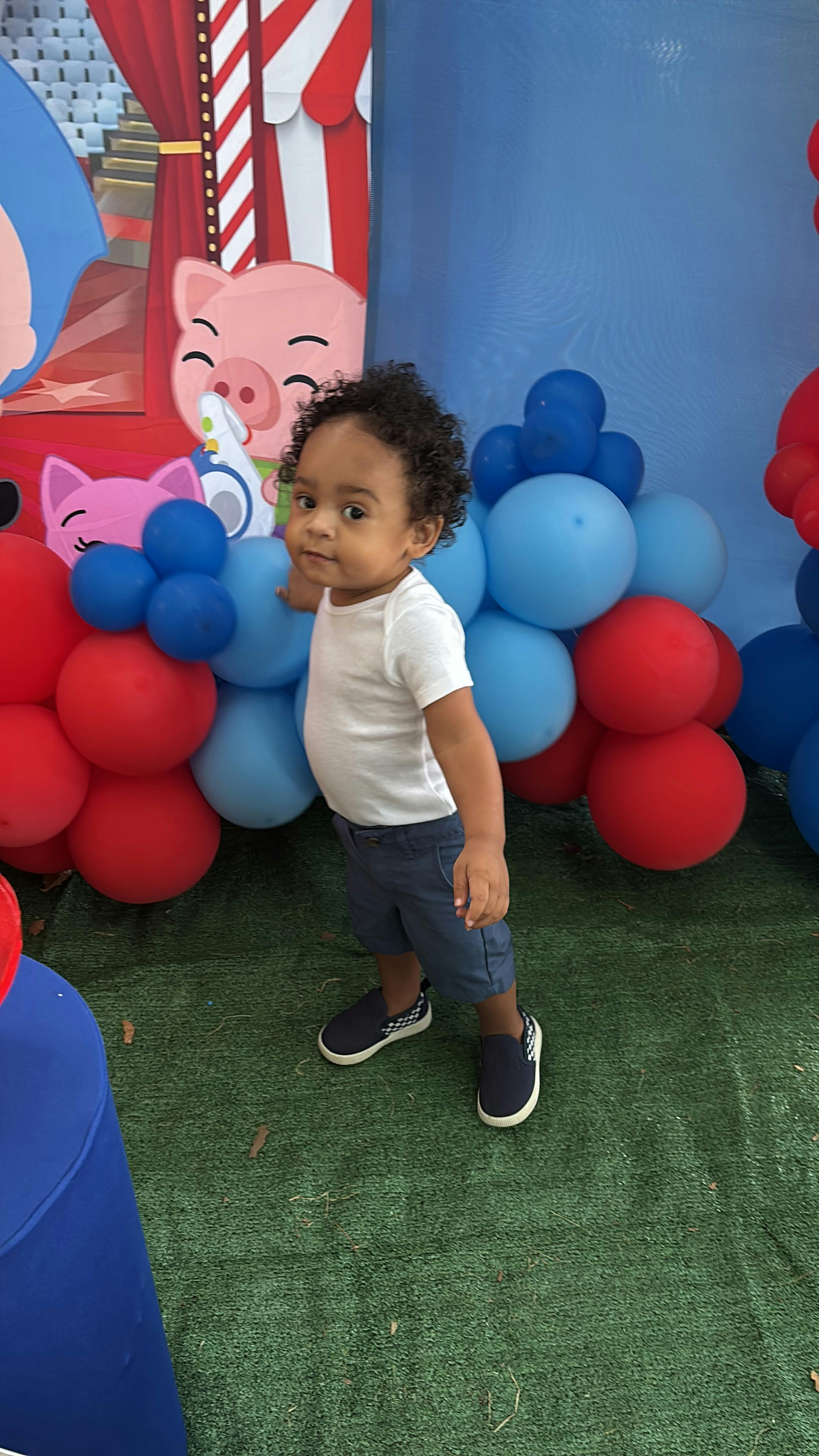 Child standing near a balloon display and a cartoon character backdrop