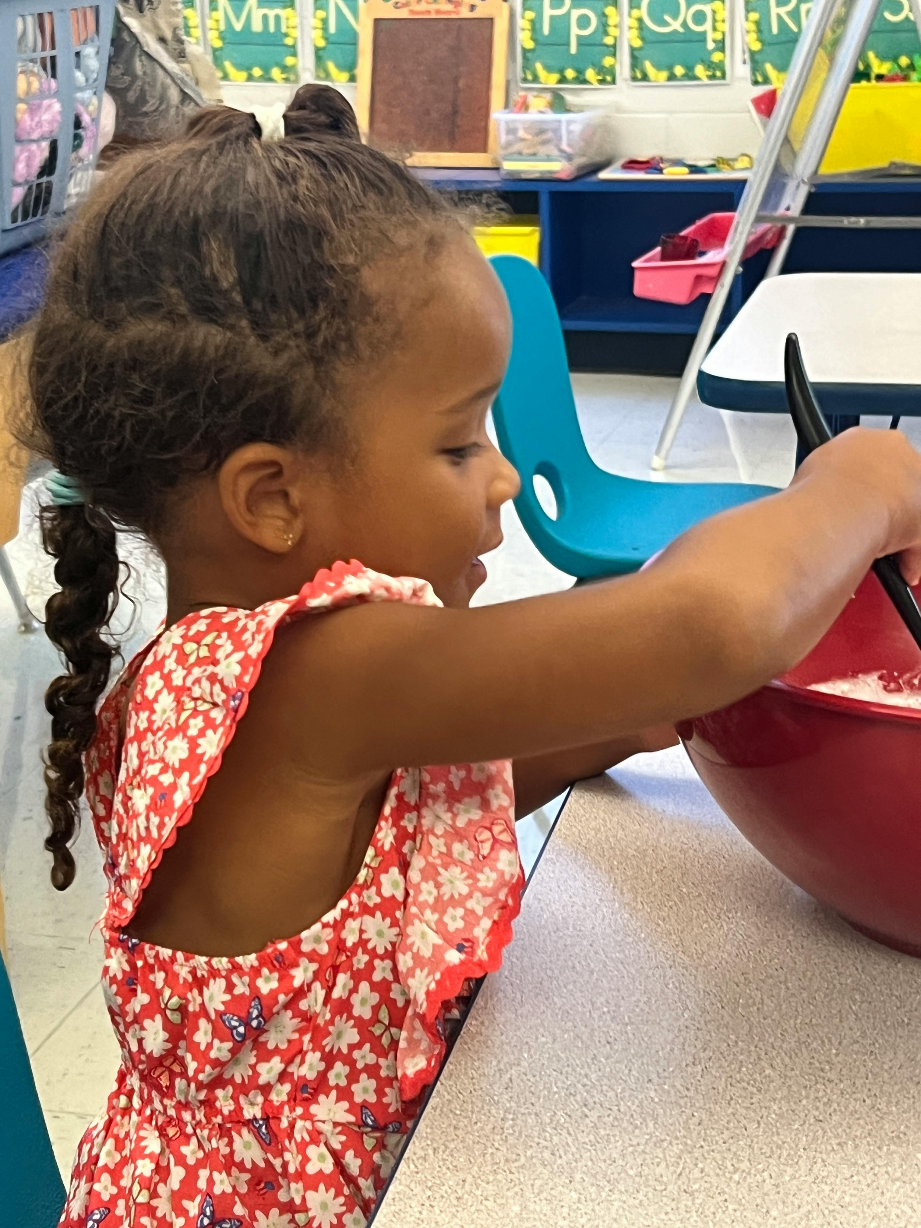 Child mixing contents in a red bowl in a classroom
