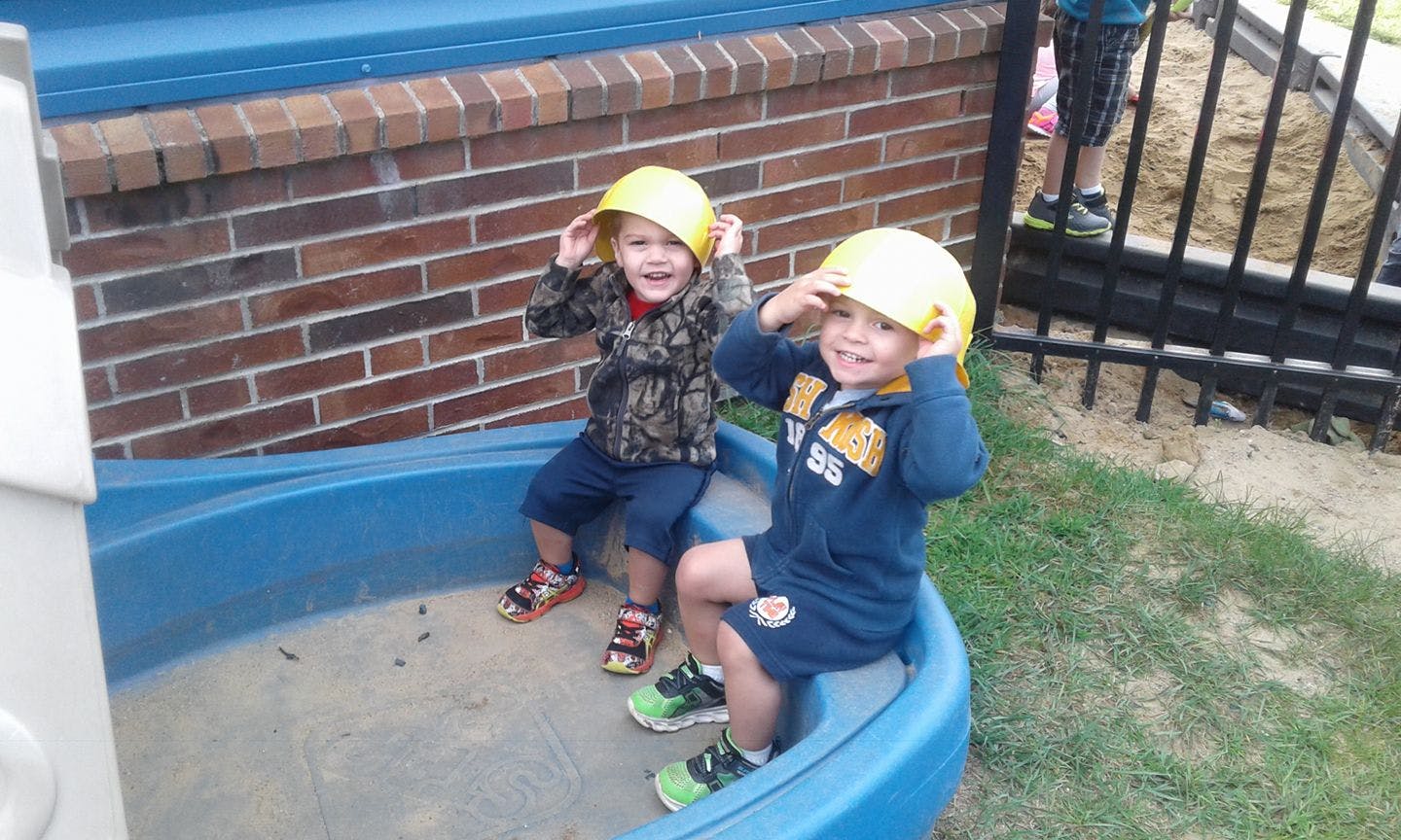 Two children wearing yellow hard hats in a sandbox