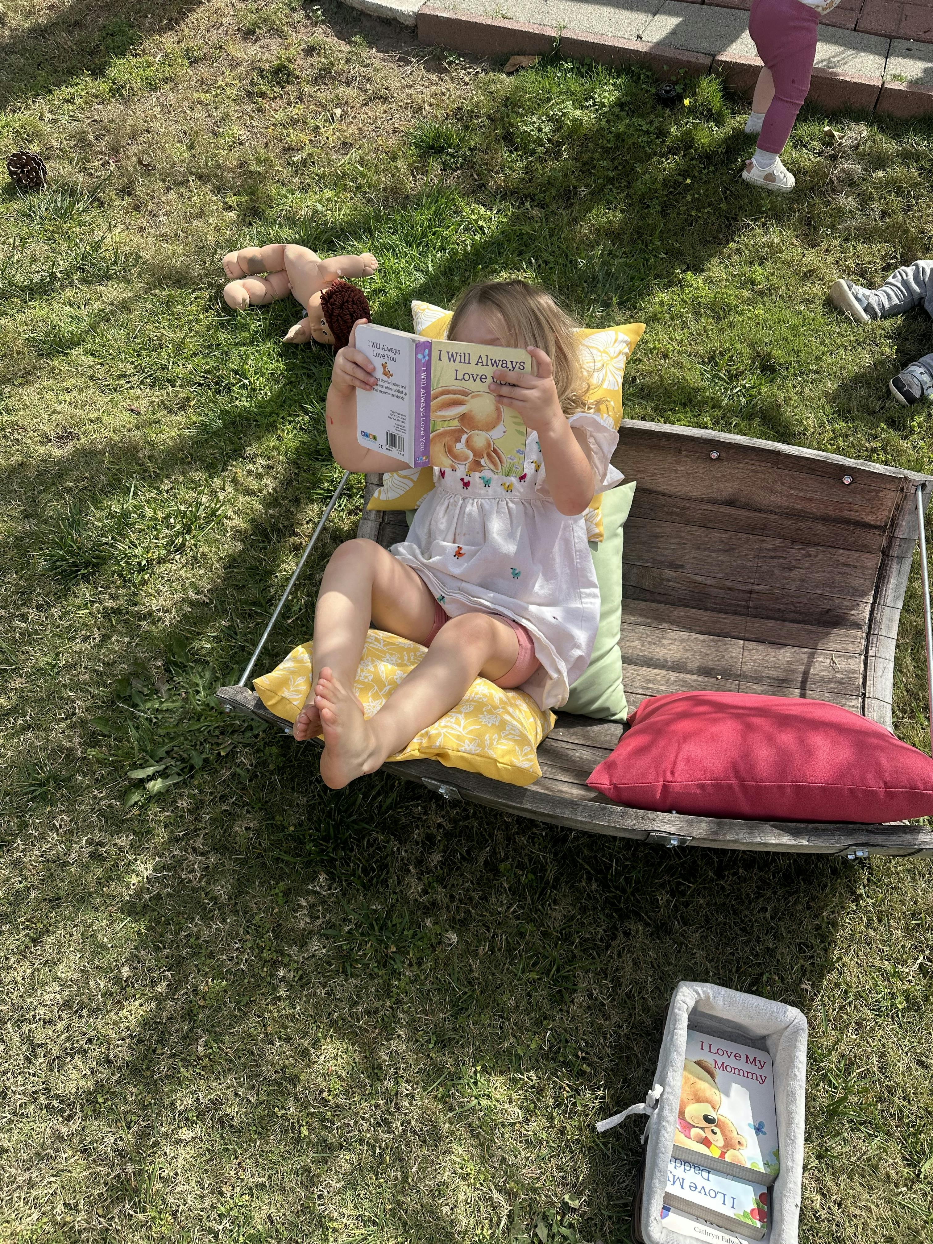 Child sitting on pillows, reading a book titled "I Will Always Love You"