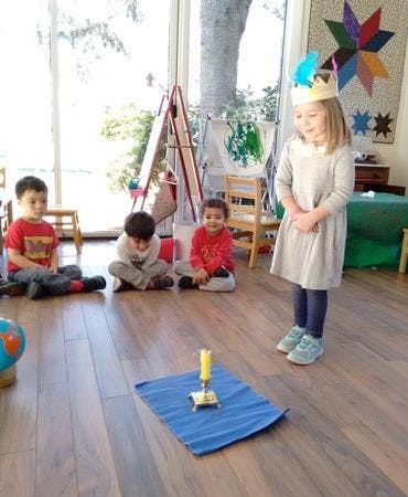 Child in crown standing in front of three seated children in a classroom