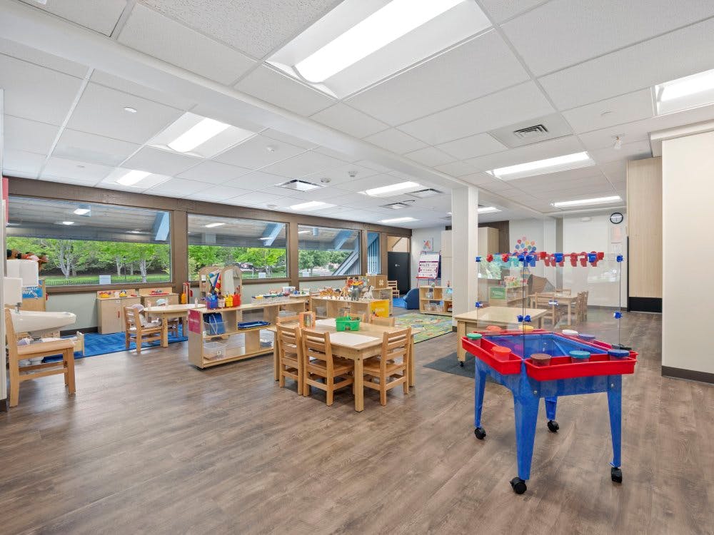 Empty classroom with small wooden tables and chairs, and a colorful play station