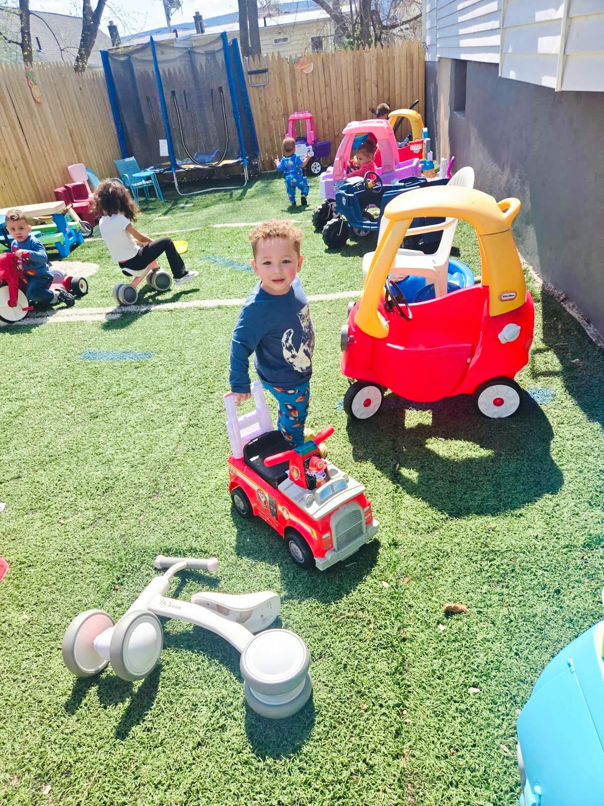 Children playing with ride-on toys in a fenced backyard