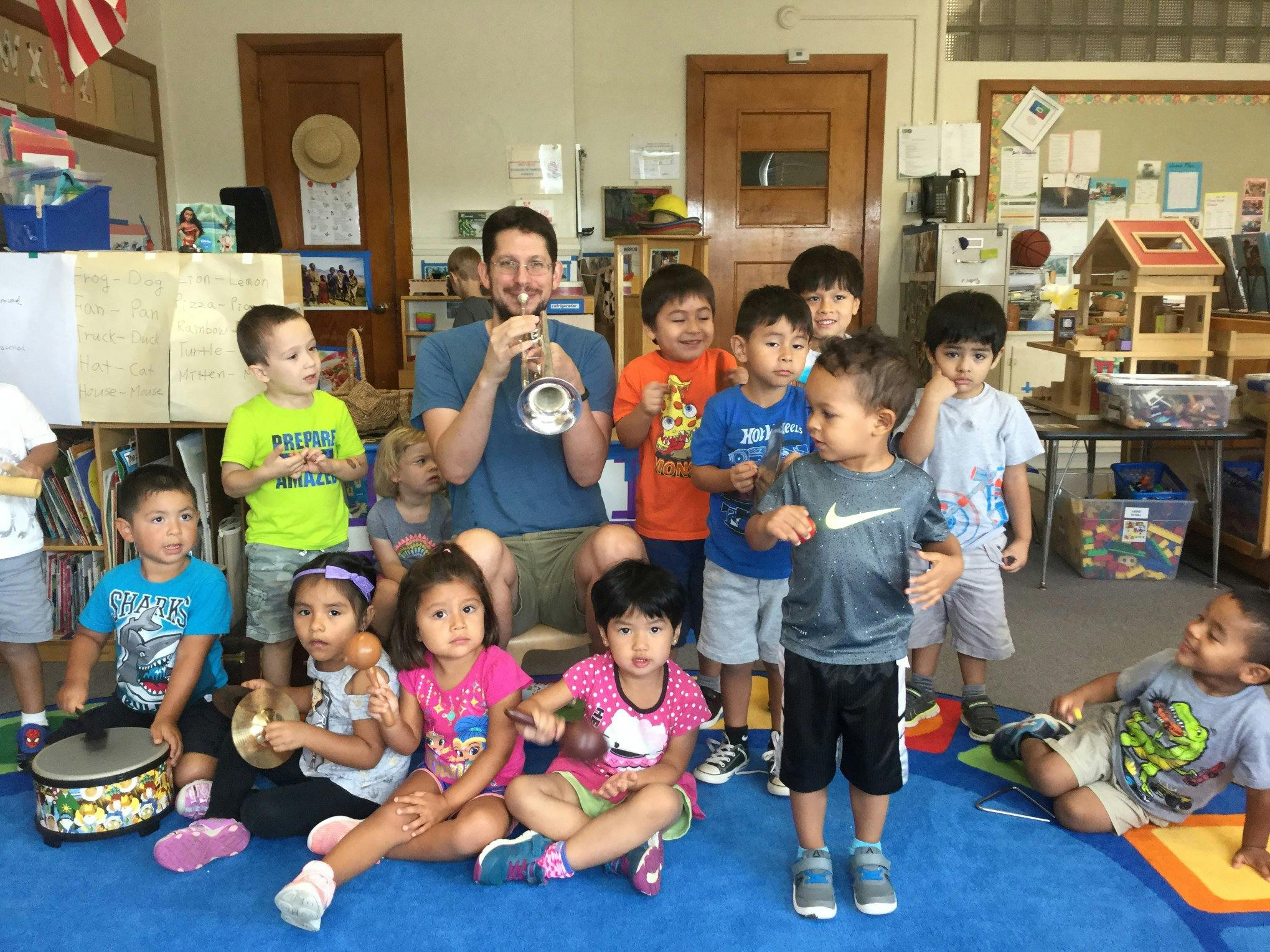 Adult playing trumpet for children with musical instruments in a classroom