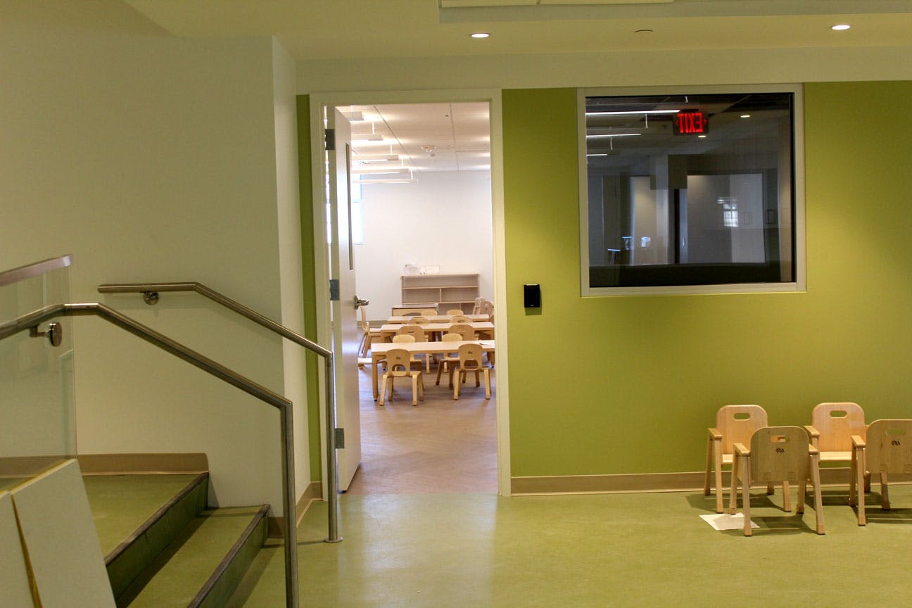 Classroom with small tables and chairs visible through an open doorway