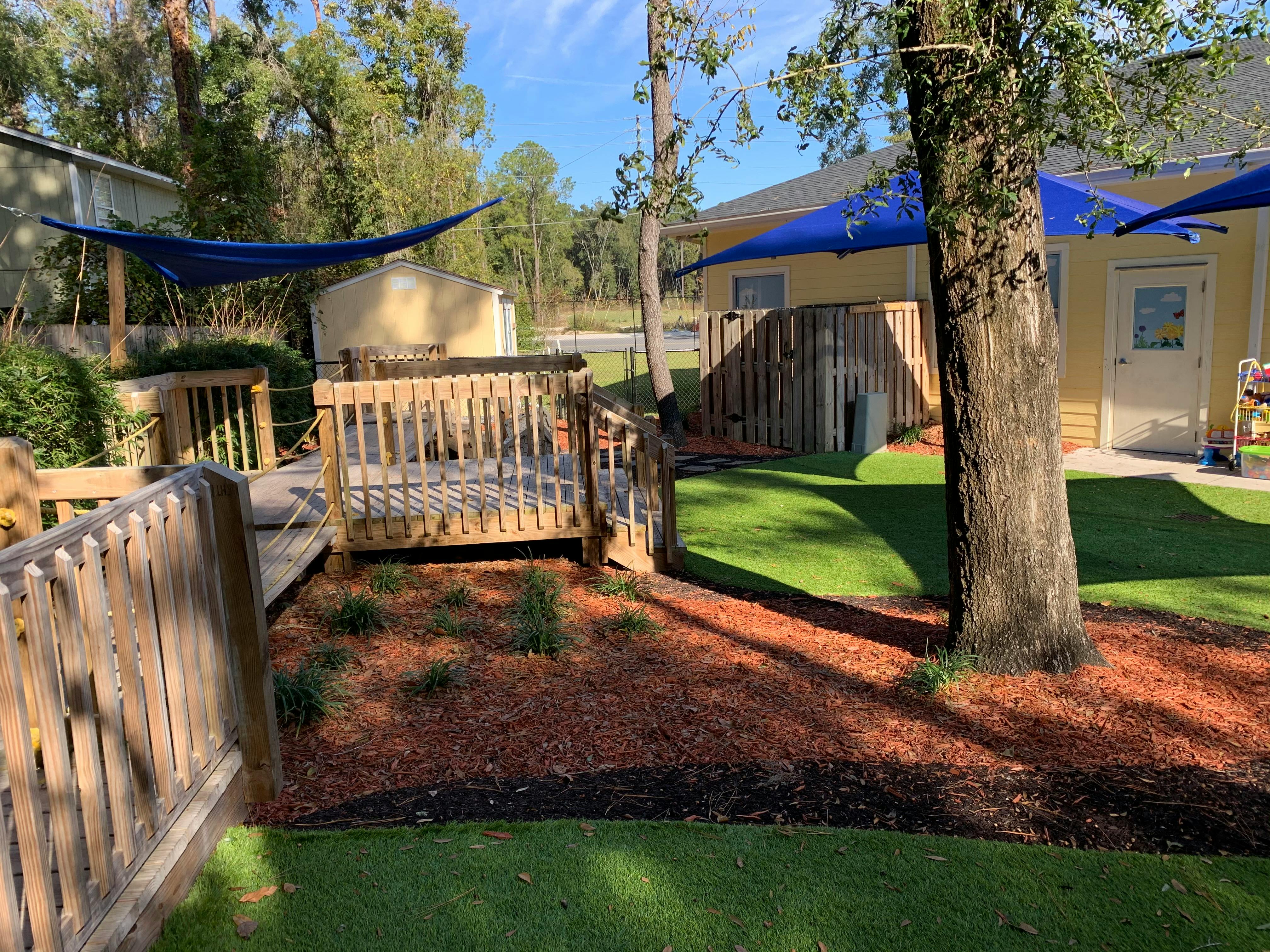 Outdoor play area with wooden platforms, artificial grass, and blue shade tarps