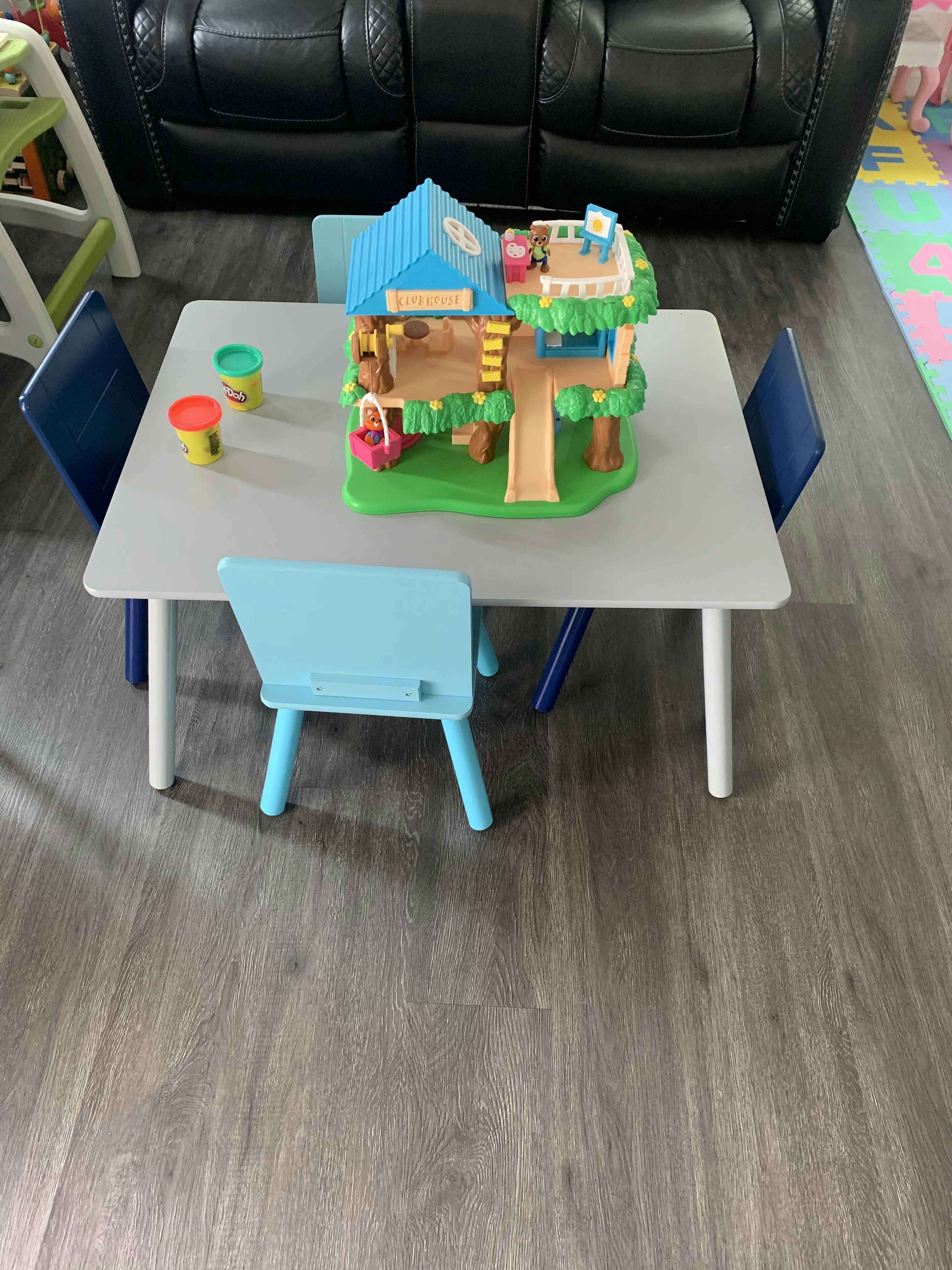 Toy treehouse and play-doh containers on a child's table with chairs