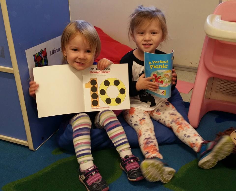 Two children sitting on the floor, one holding a book with the number 10
