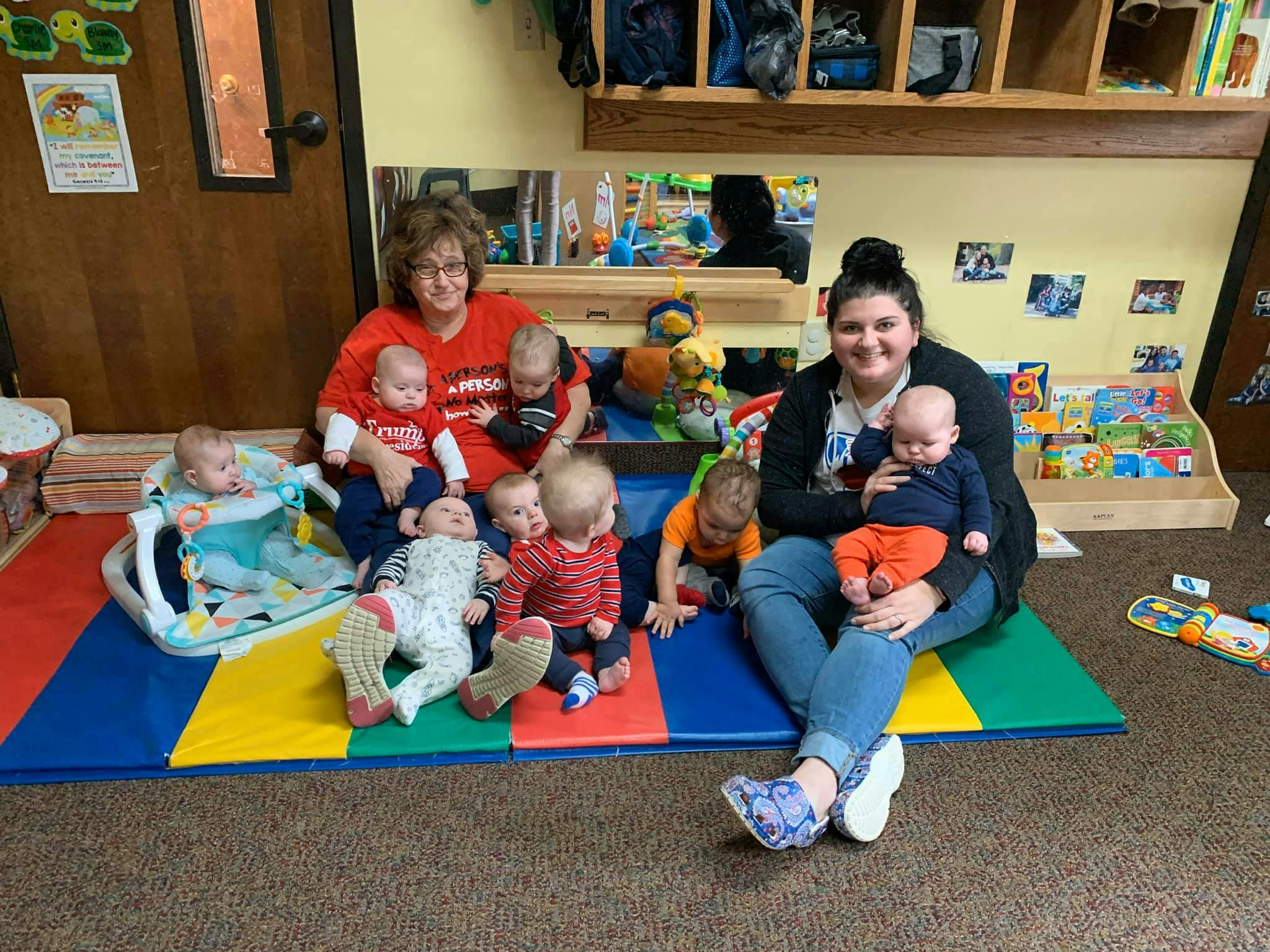 Two people with multiple babies and young children in a classroom