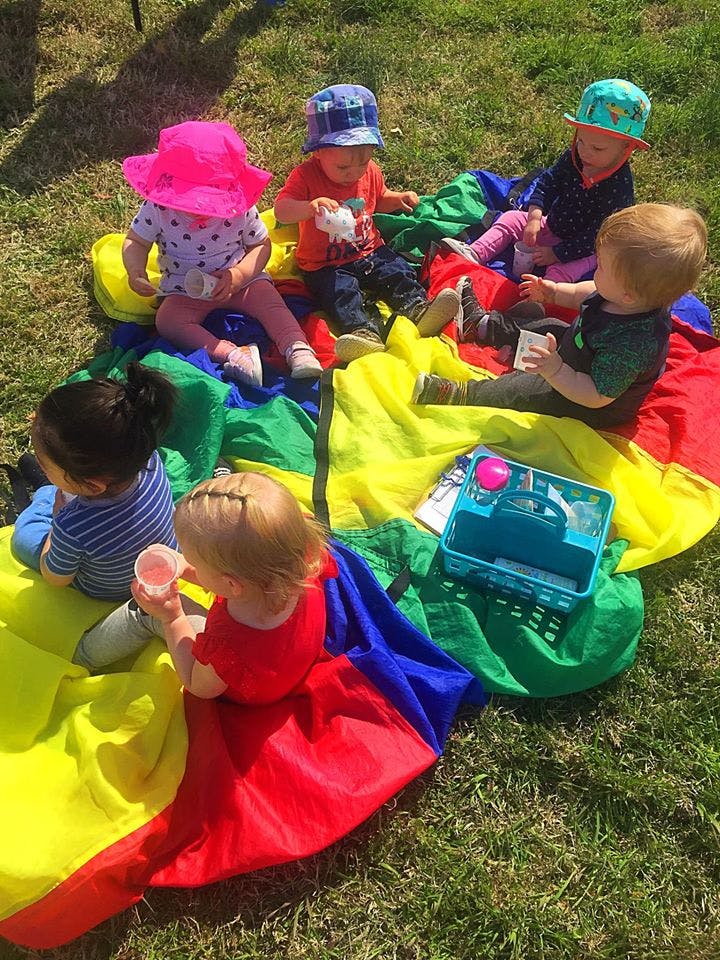 Several children sitting on a colorful parachute on grass