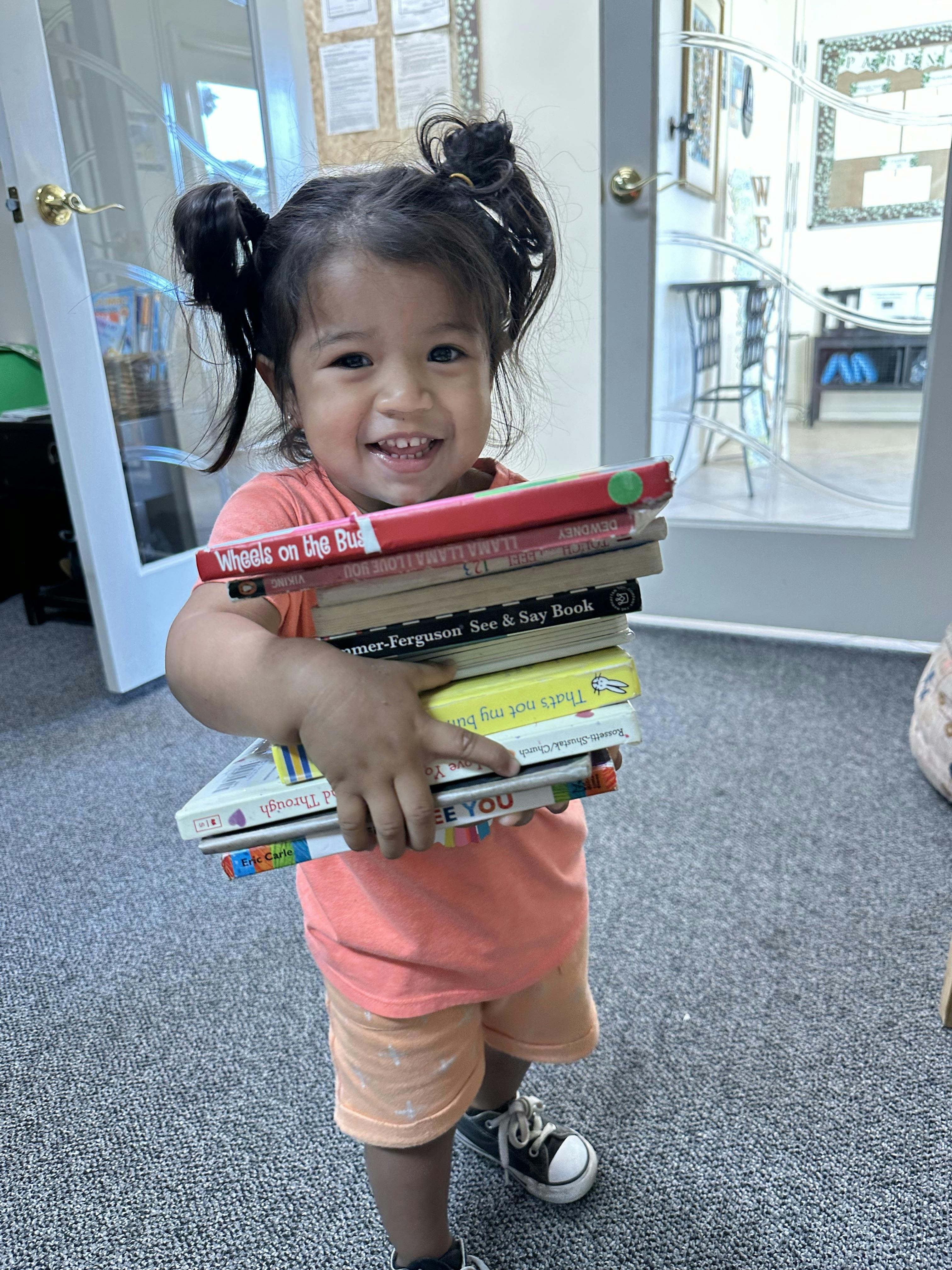 Child smiling while holding a stack of books