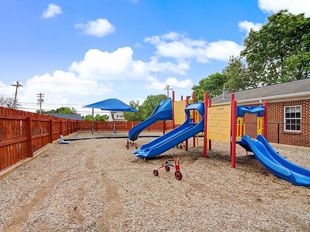 Empty outdoor playground with blue slides, climbing structures, and a red fence
