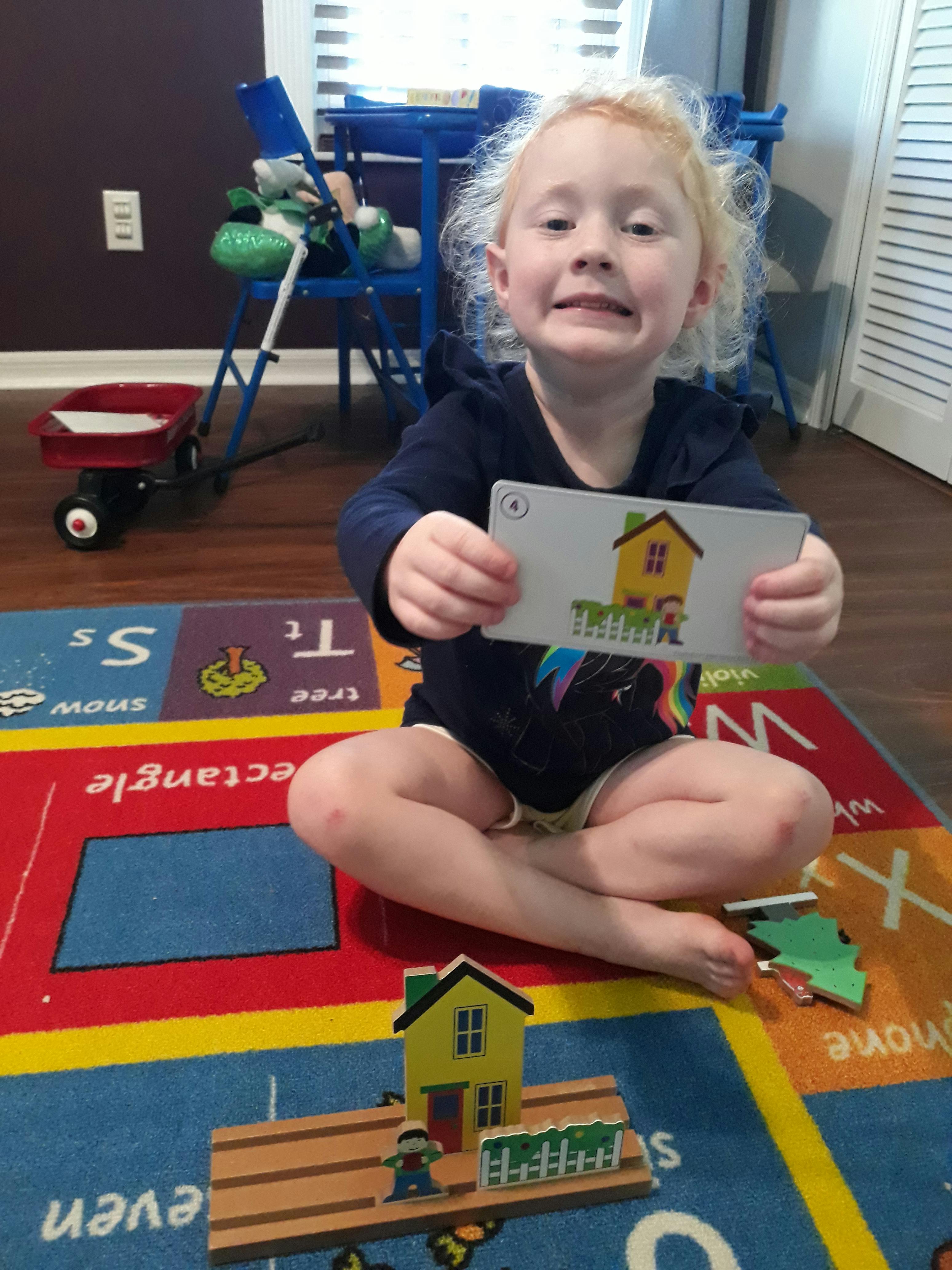Child sitting on a rug holding up a card with a house illustration
