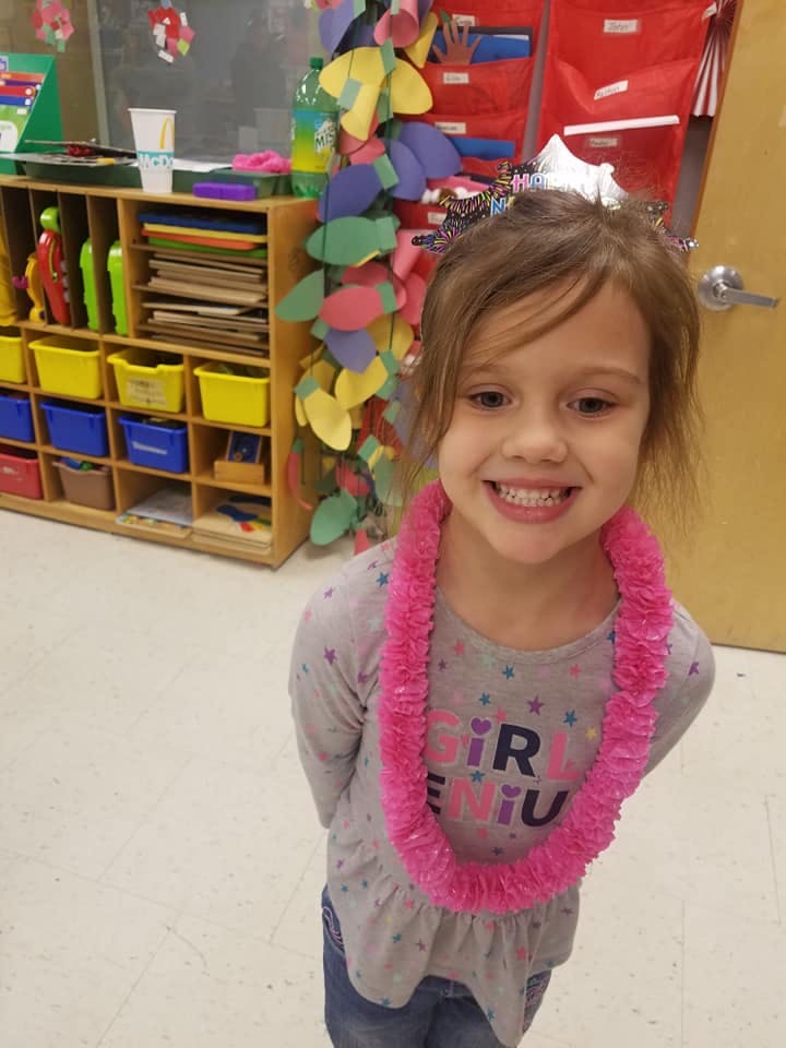 Child wearing a pink lei in a classroom