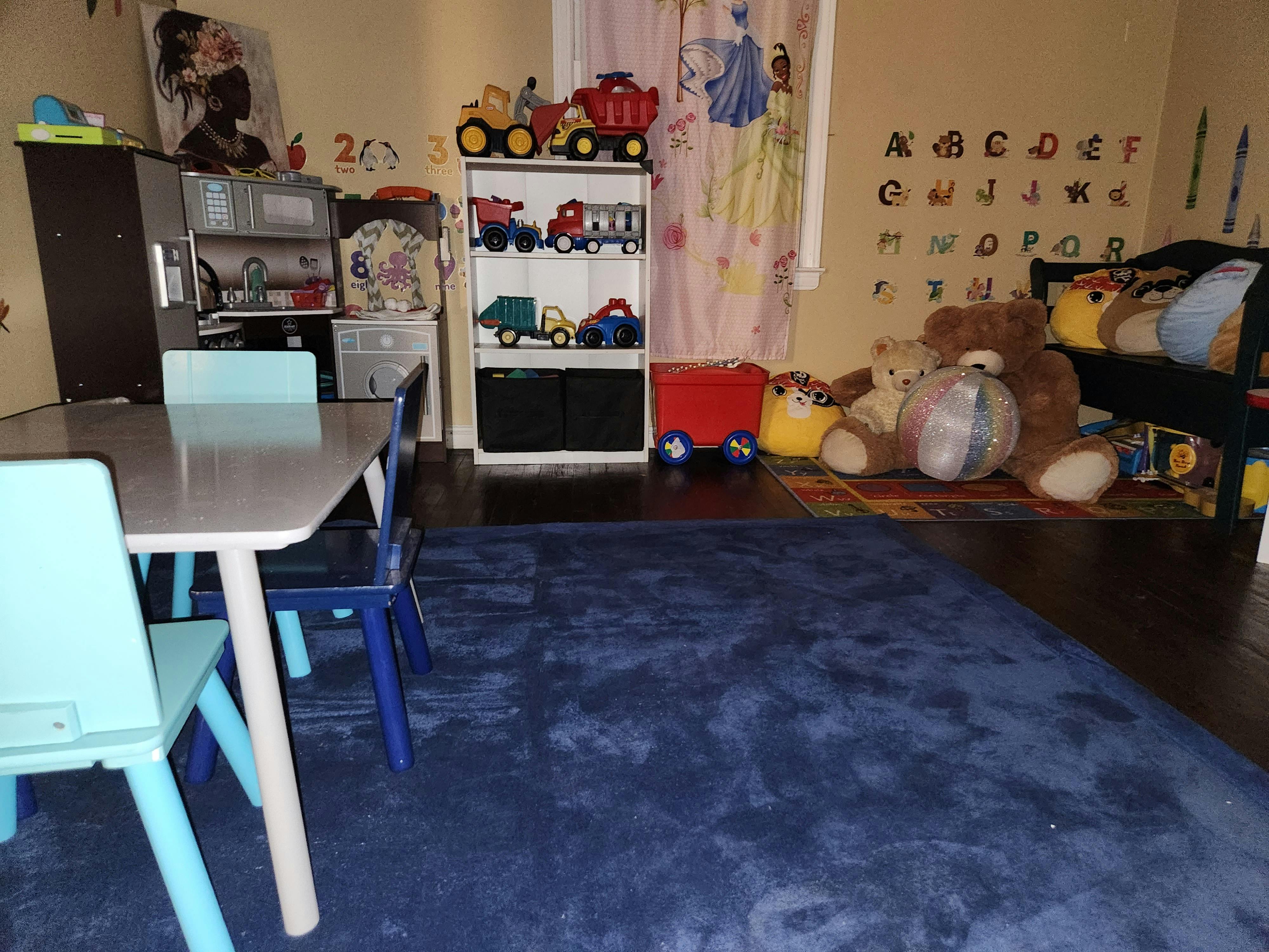 Children's playroom with a table and chairs, toy shelf, and stuffed animals