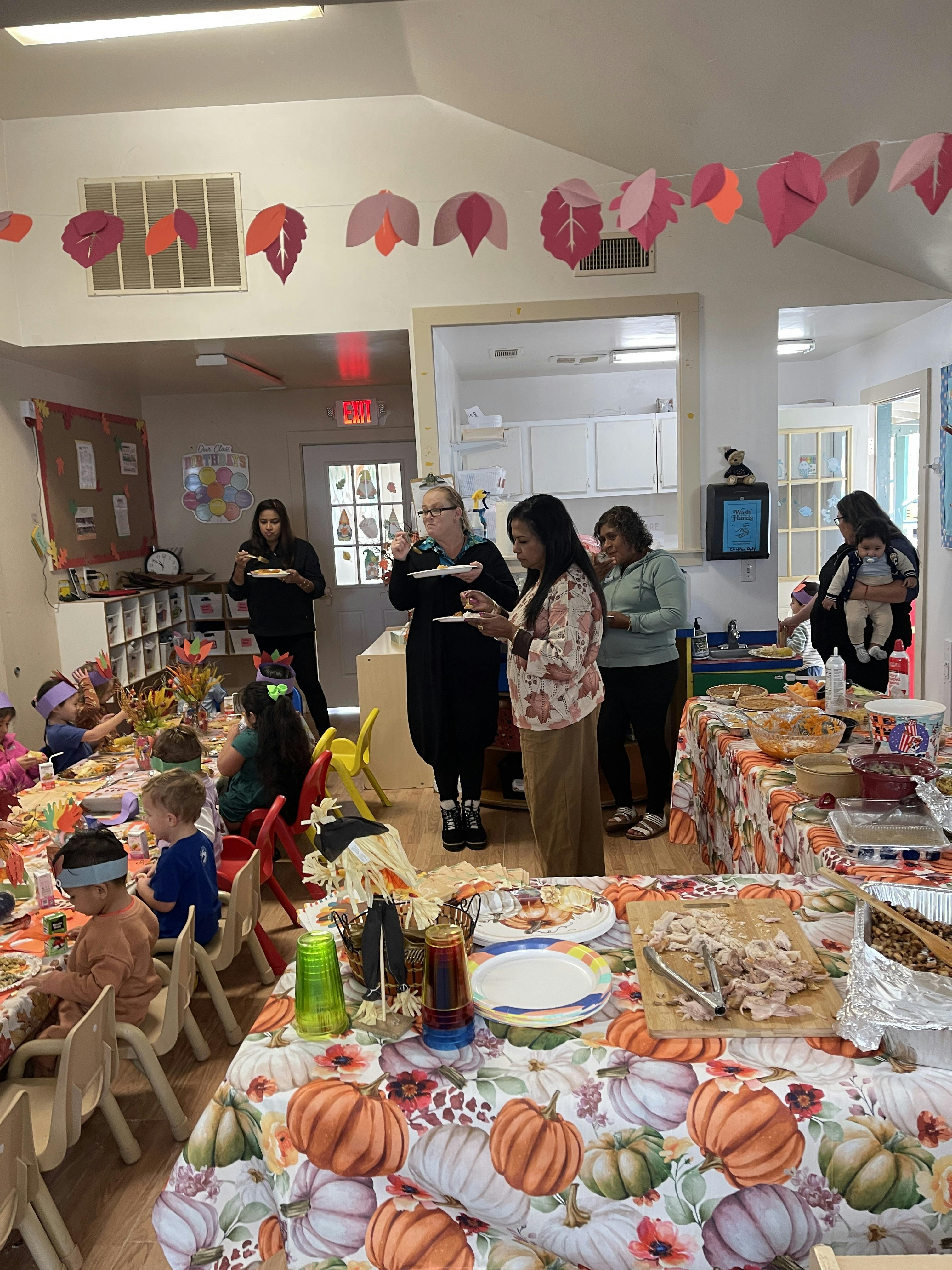 People and children gathered around tables with food, some eating