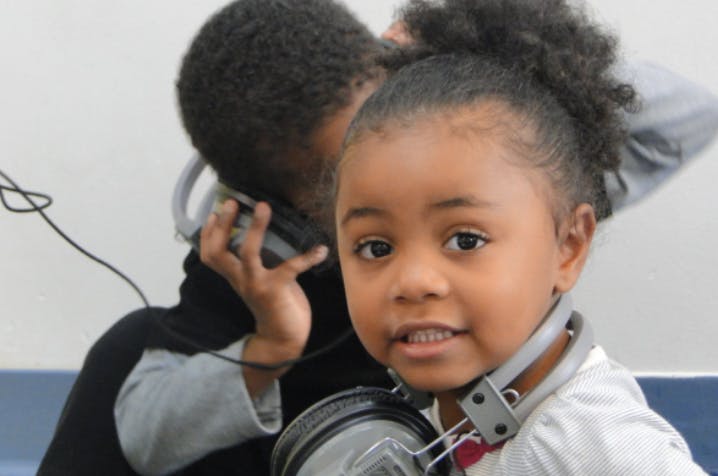 Child with headphones around neck, another child in background with headphones