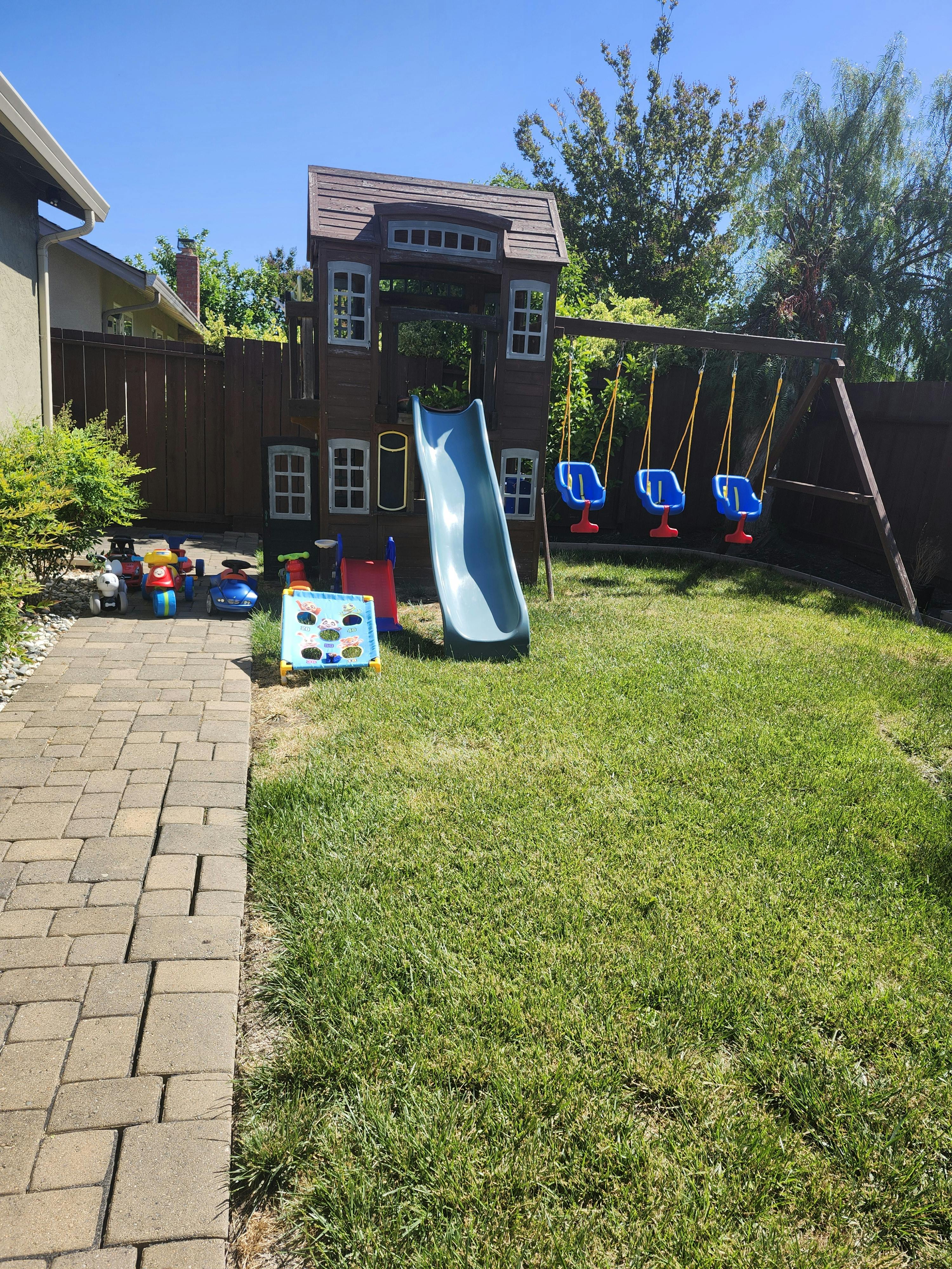 Backyard with a wooden playhouse, slide, and swing set