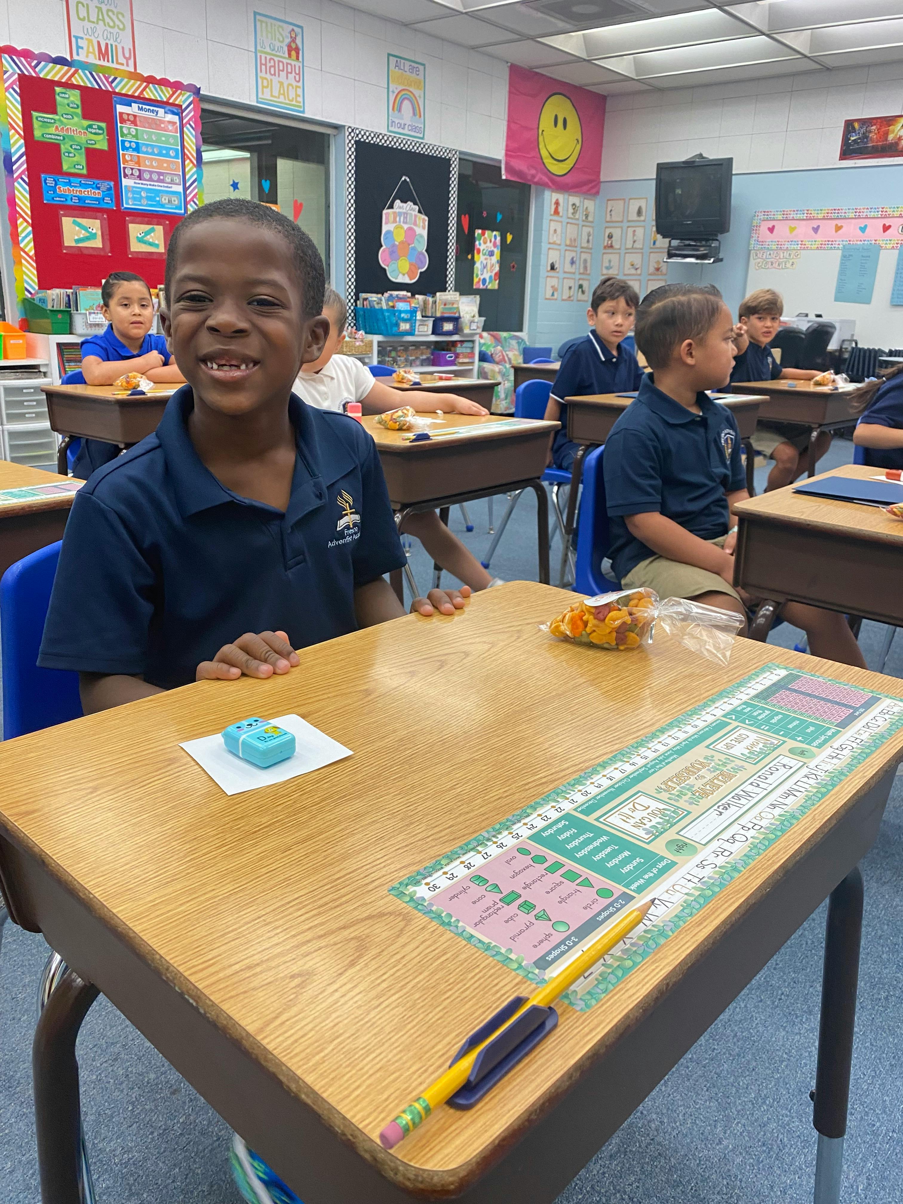 A child smiling at a desk in a classroom