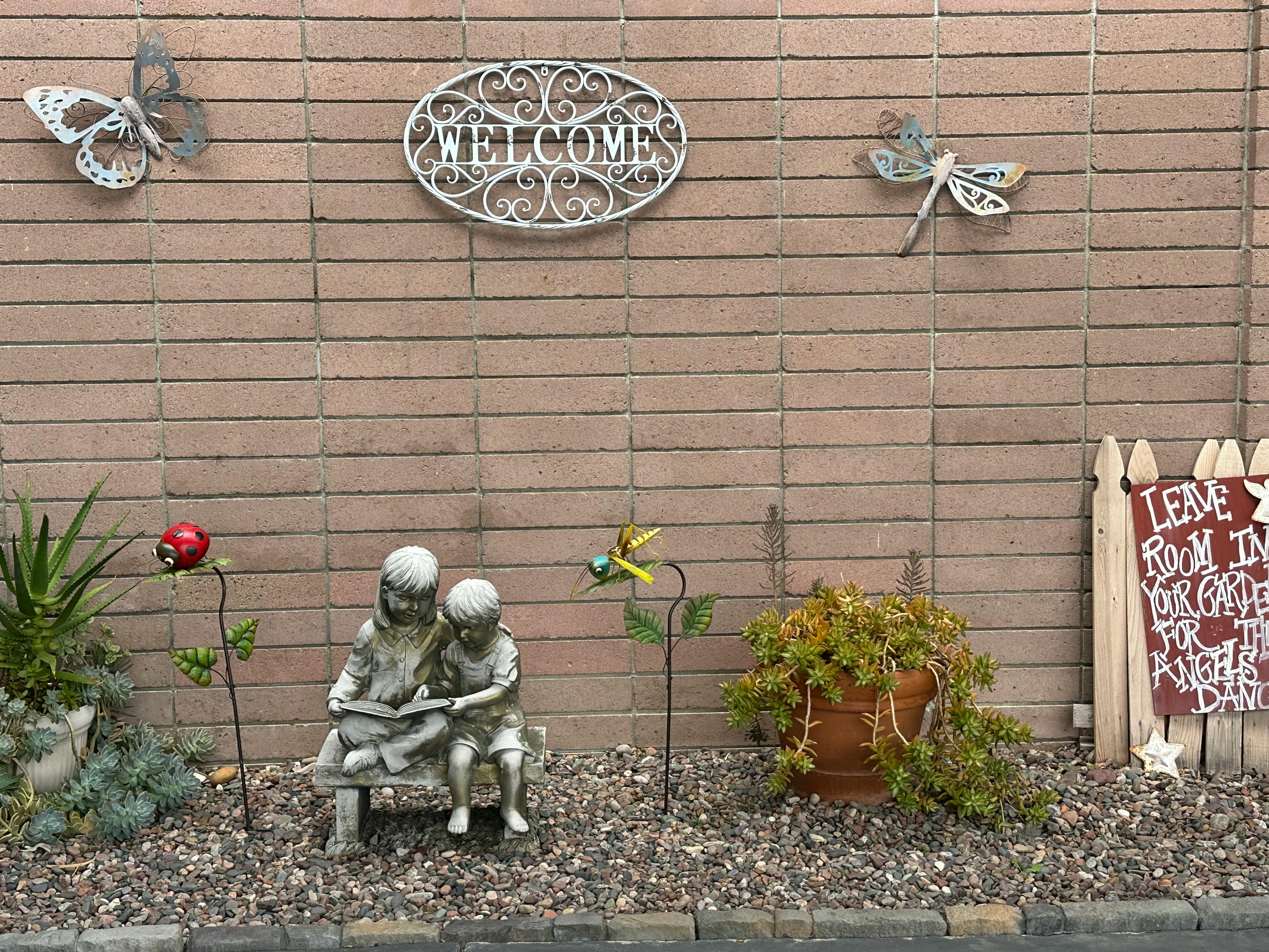 Garden decor with a statue of two children reading, a welcome sign, and plants