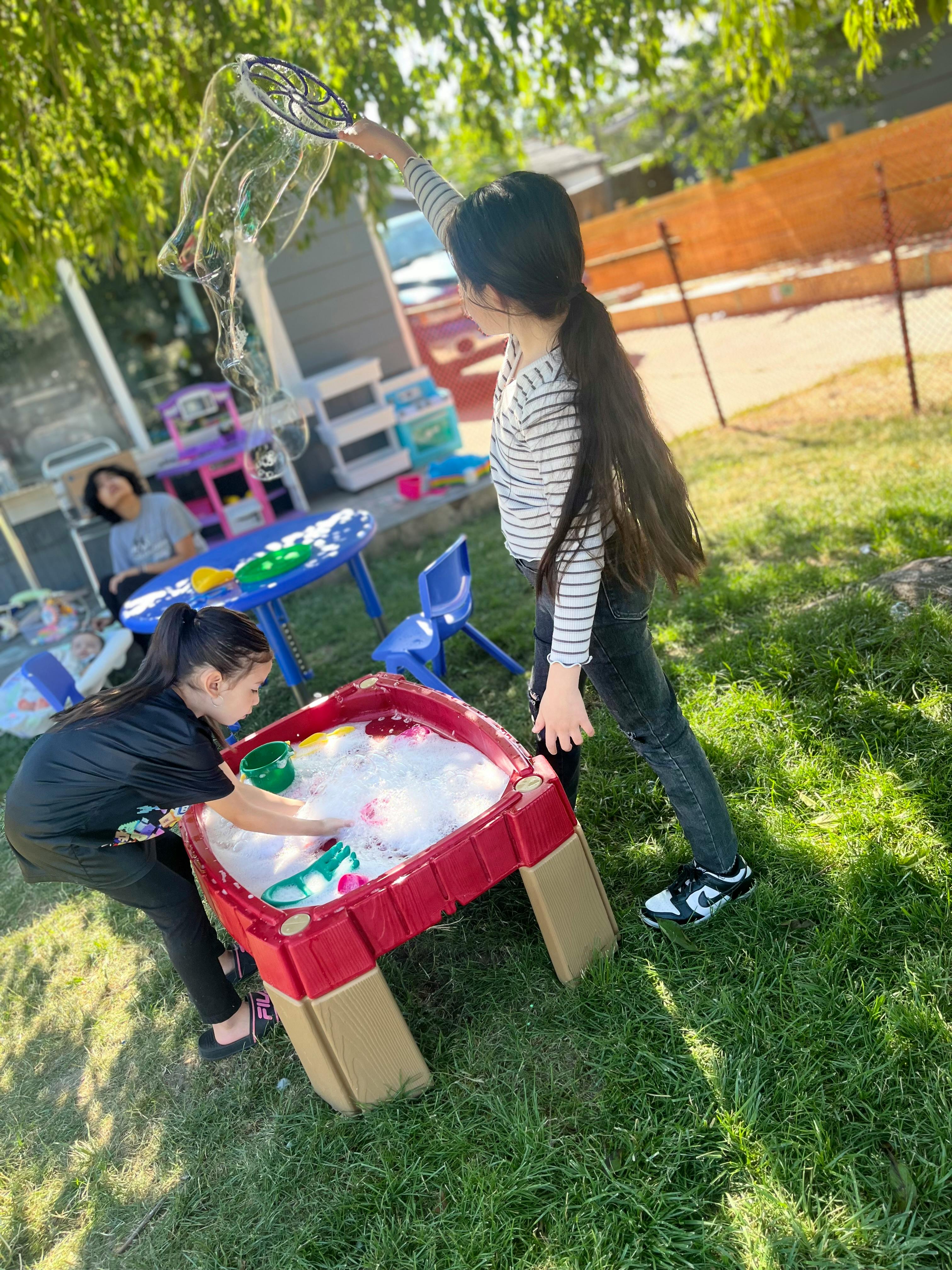 Child playing with bubbles, another child playing in a water table
