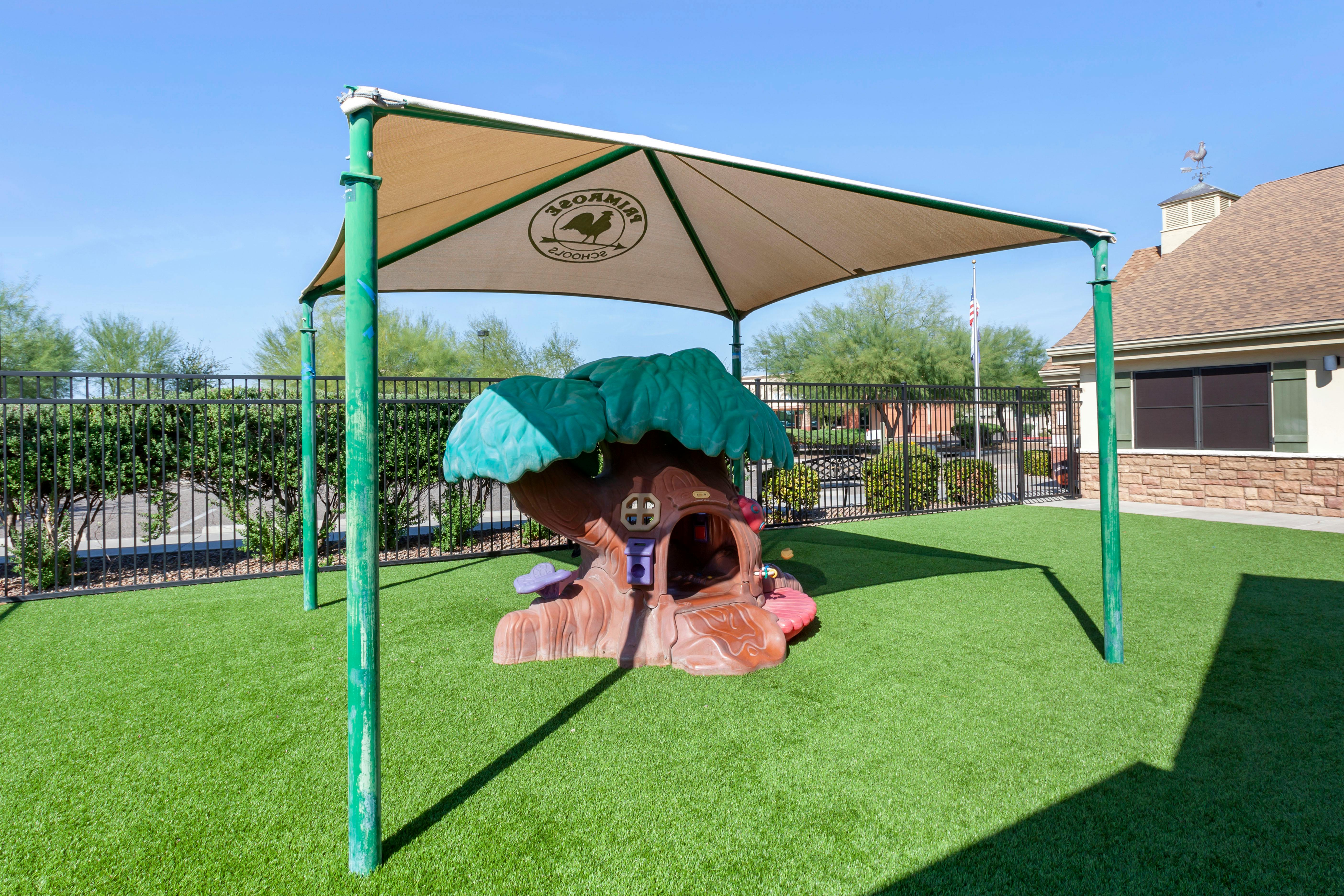 Playground with a treehouse structure under a shade canopy on artificial turf